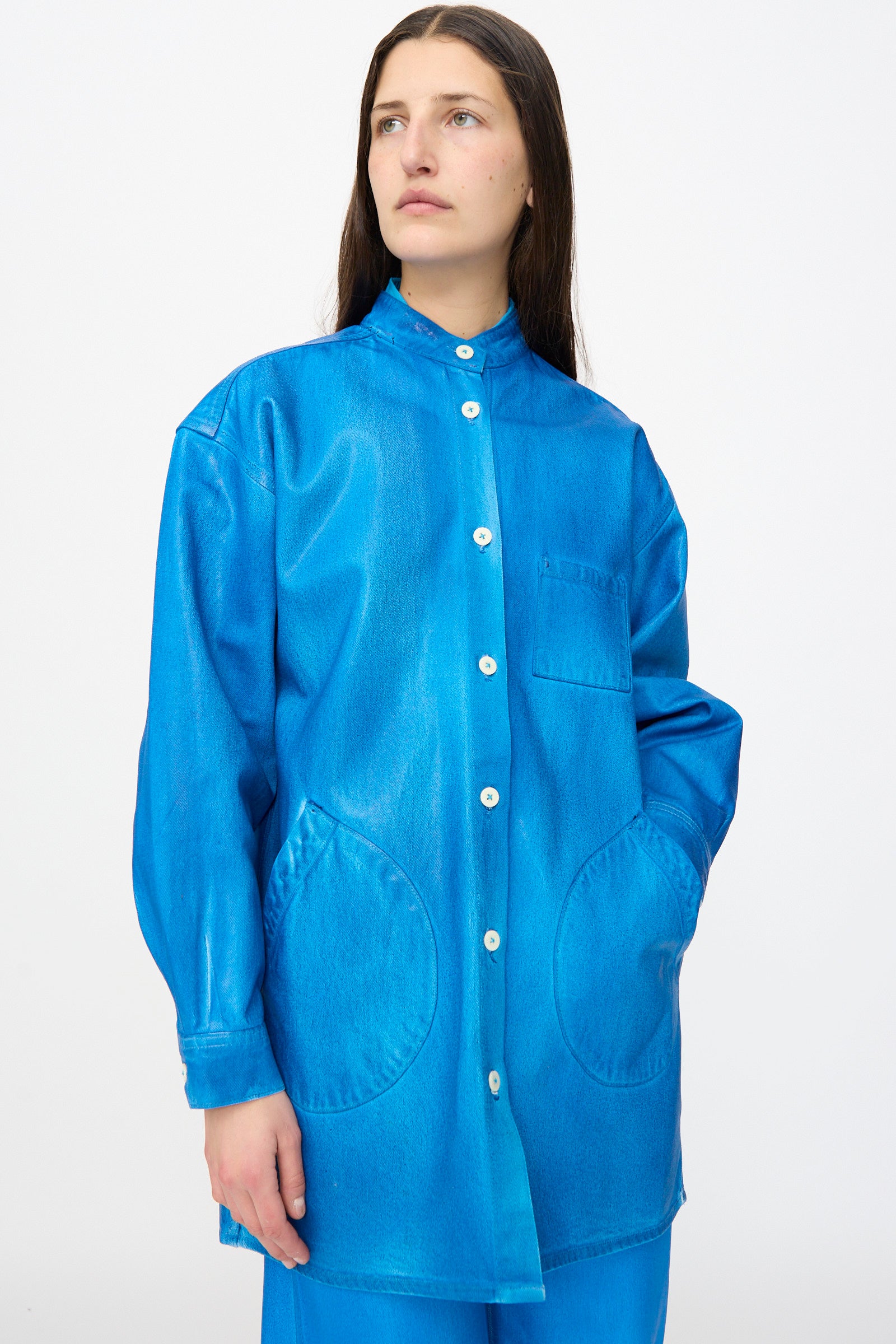 A woman models the Jesse Kamm Band Collar Okuda Jacket in Electric Blue Lacquer, a loose-fitting denim jacket with large pockets, set against a plain white background.