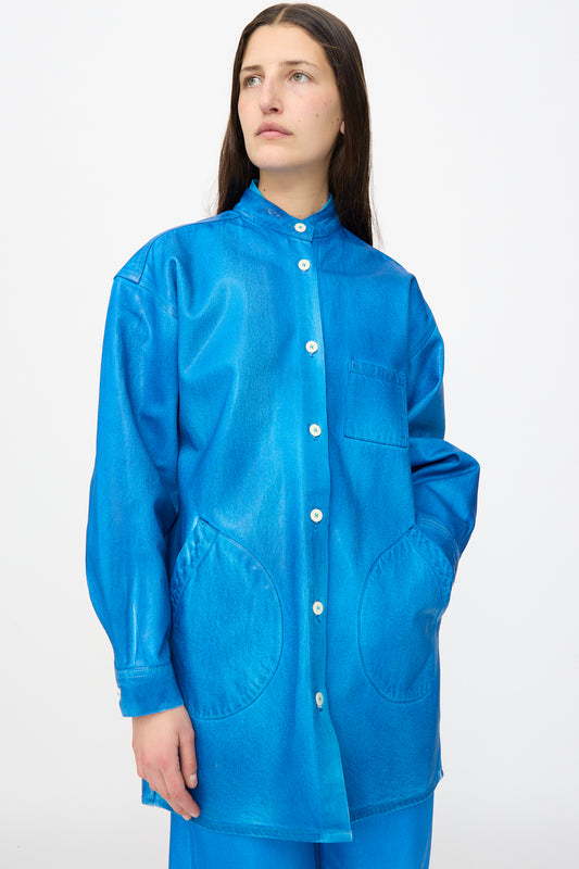 A woman models the Jesse Kamm Band Collar Okuda Jacket in Electric Blue Lacquer, a loose-fitting denim jacket with large pockets, set against a plain white background.