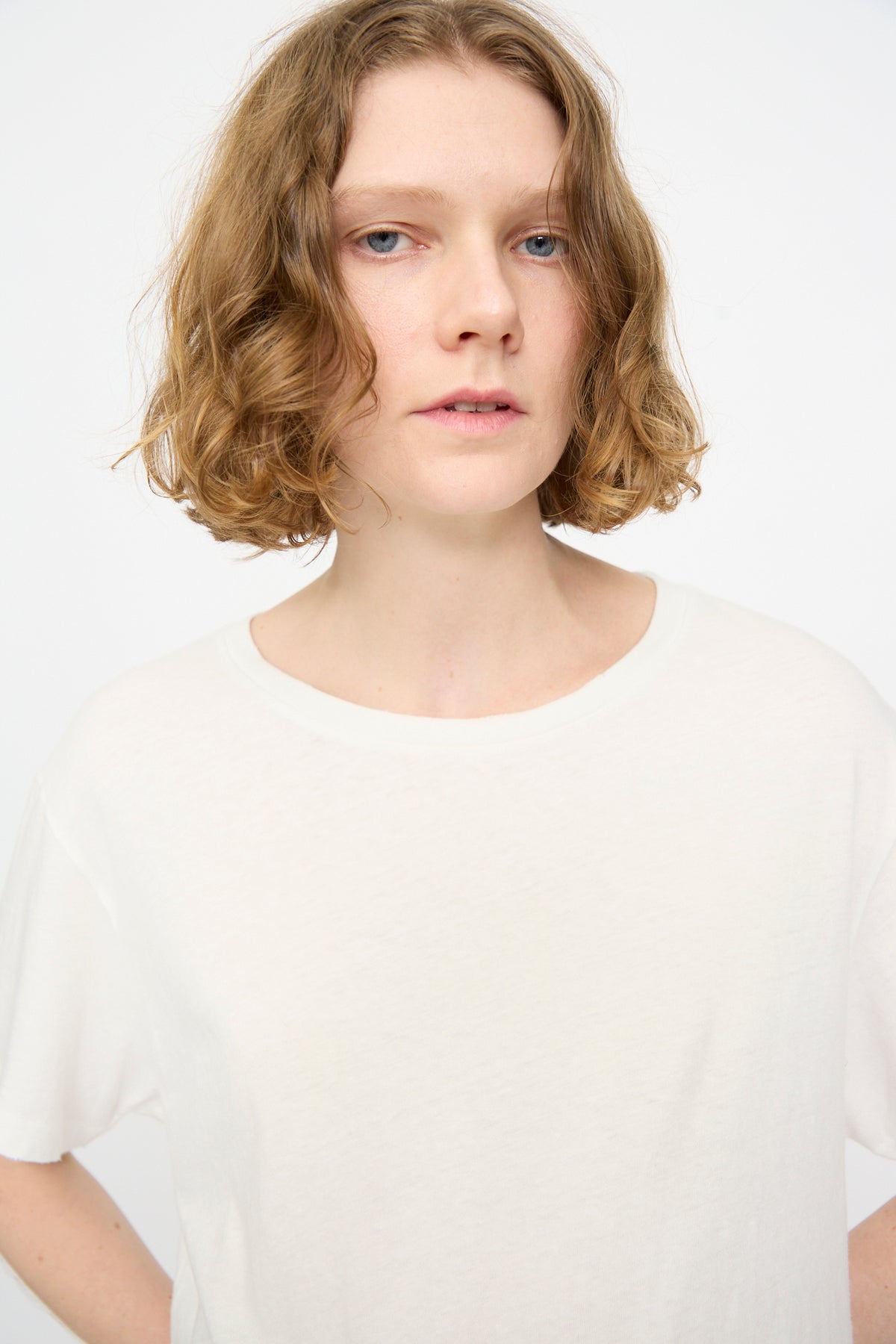 A person with short, curly light brown hair wears the Jesse Kamm Bowery Tee in Salt White and looks at the camera against a white background.