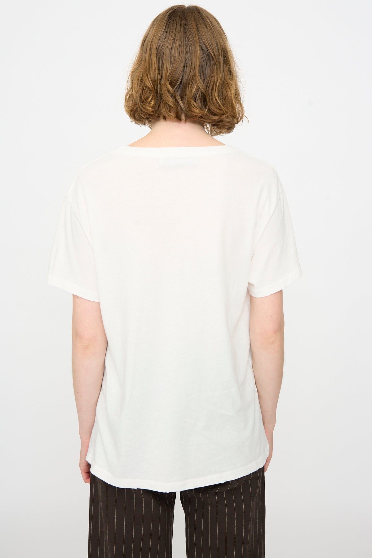 Person with short, light brown hair wearing the Jesse Kamm Bowery Tee in Salt White and dark pinstripe pants, shown from the back against a plain white background.