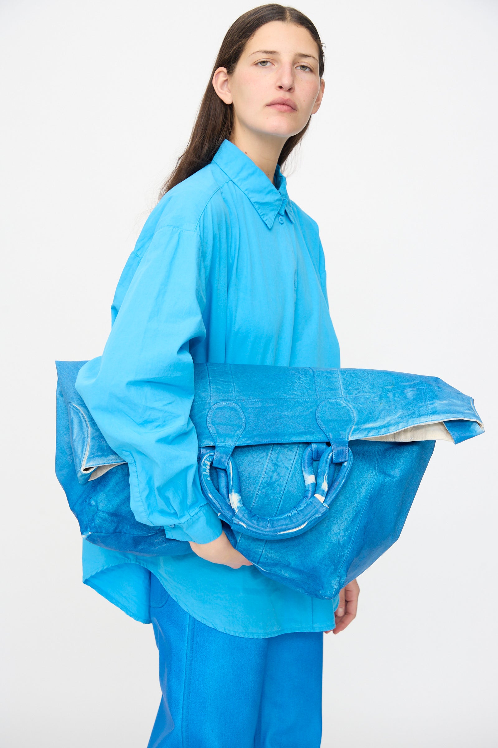 A model wears an oversized bright blue shirt and pants, holding the Jesse Kamm Canvas Big Bag in Electric Blue Lacquer against a plain white background.