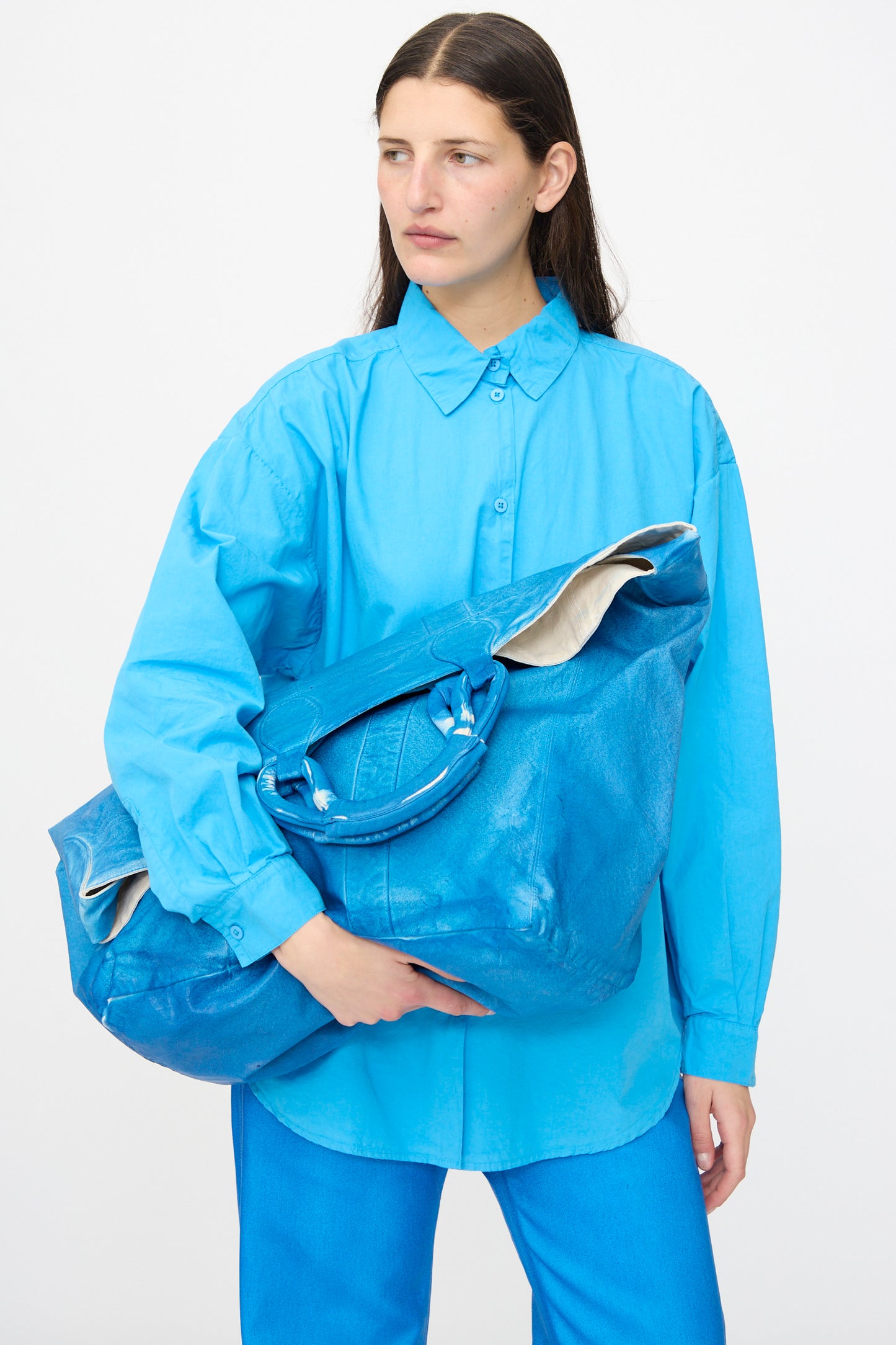 A person in a bright blue outfit holds the Jesse Kamm Canvas Big Bag in Electric Blue Lacquer against a plain white background.