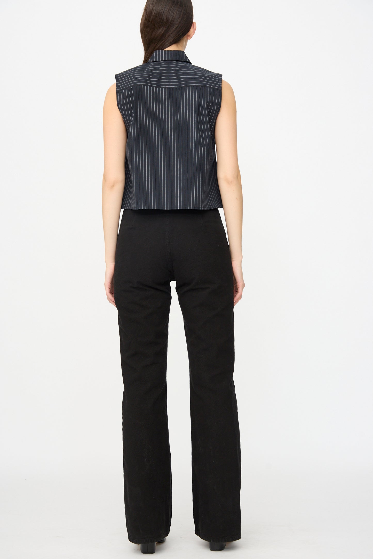 A person stands facing away against a plain white background, wearing the Jesse Kamm Canvas Les Deux Pants in Black with a matching black pinstriped sleeveless top, both crafted from organic cotton canvas.