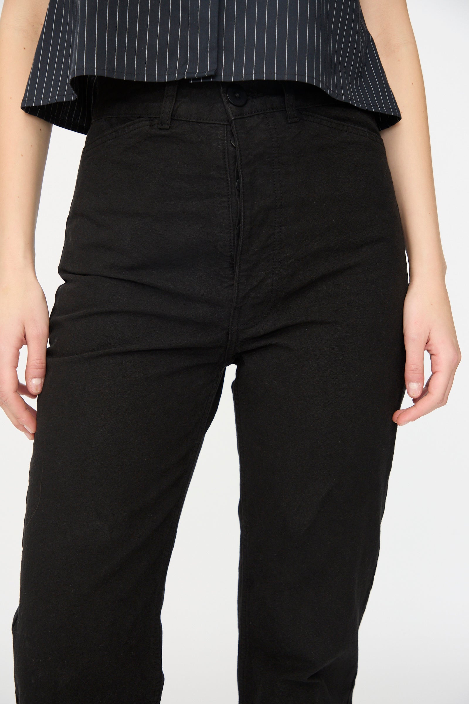 Person wearing Jesse Kamm Canvas Les Deux Pants in Black—crafted from organic cotton canvas and made in California—with a black shirt featuring white pinstripes, standing with arms relaxed at their sides.