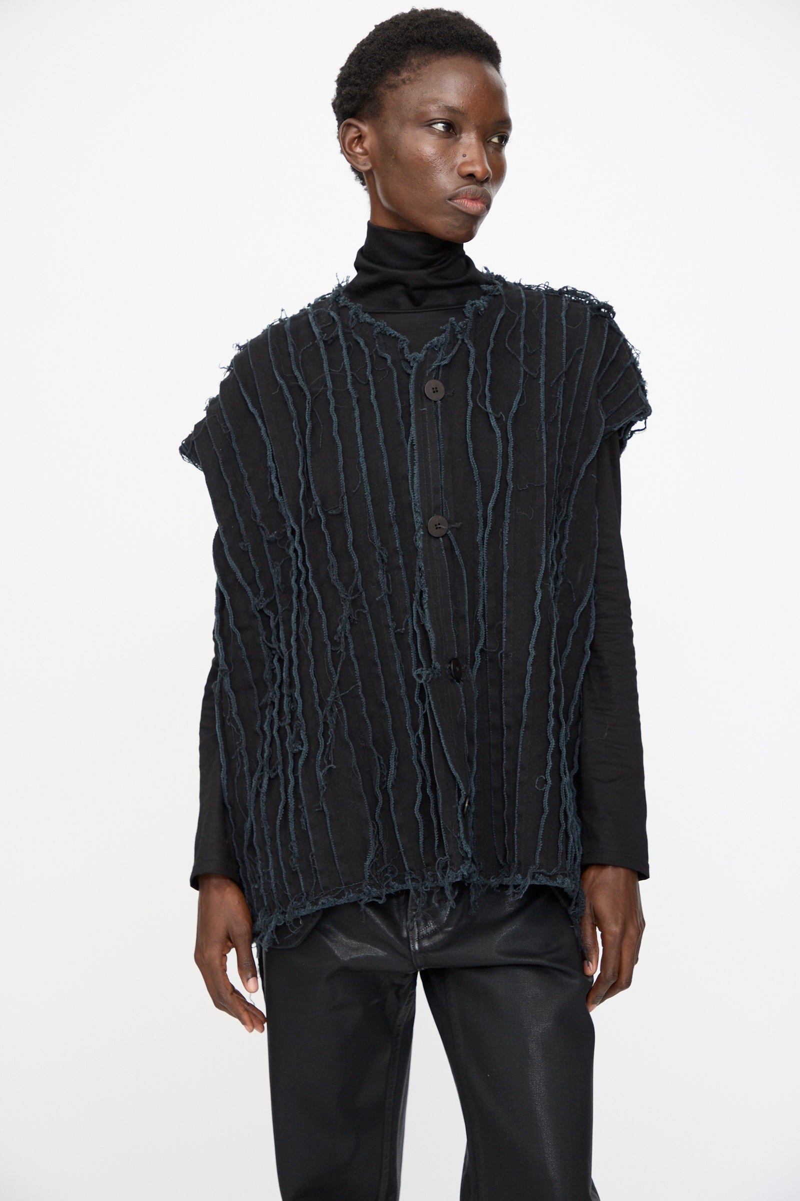 Person wearing the Deadstock 10oz. Denim Baleen Vest in Black by Jesse Kamm over a black turtleneck and black pants, standing against a plain white background.