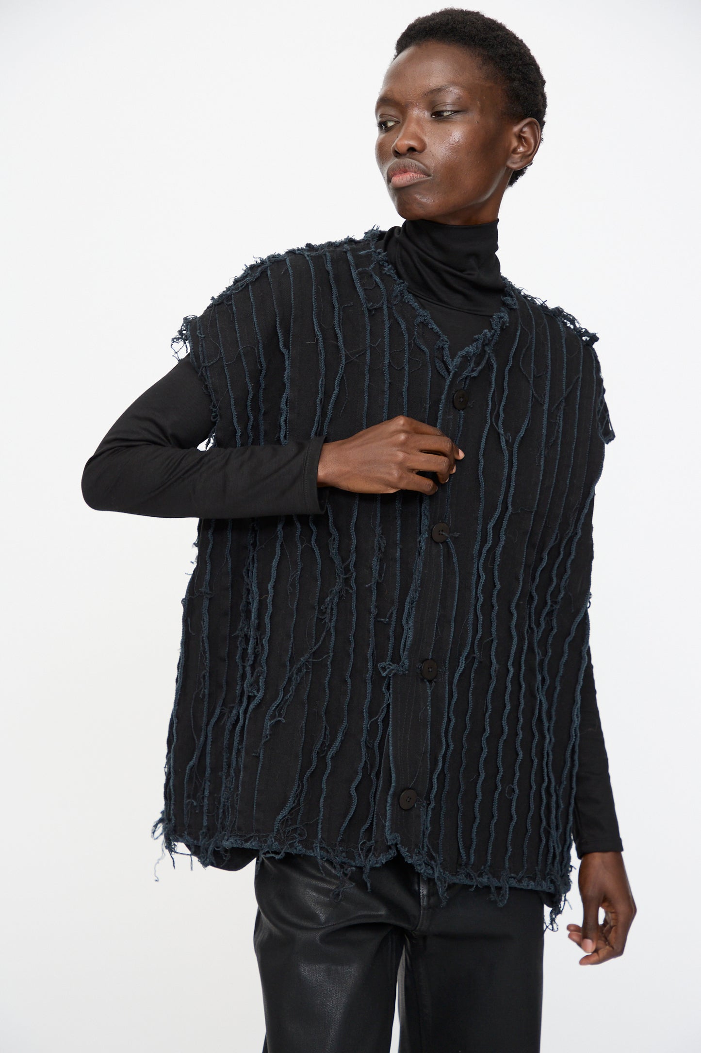 Model wears Jesse Kamm’s Deadstock 10oz. Denim Baleen Vest in Black with a black turtleneck and pants, featuring textured, fringed details, styled against a plain white background.