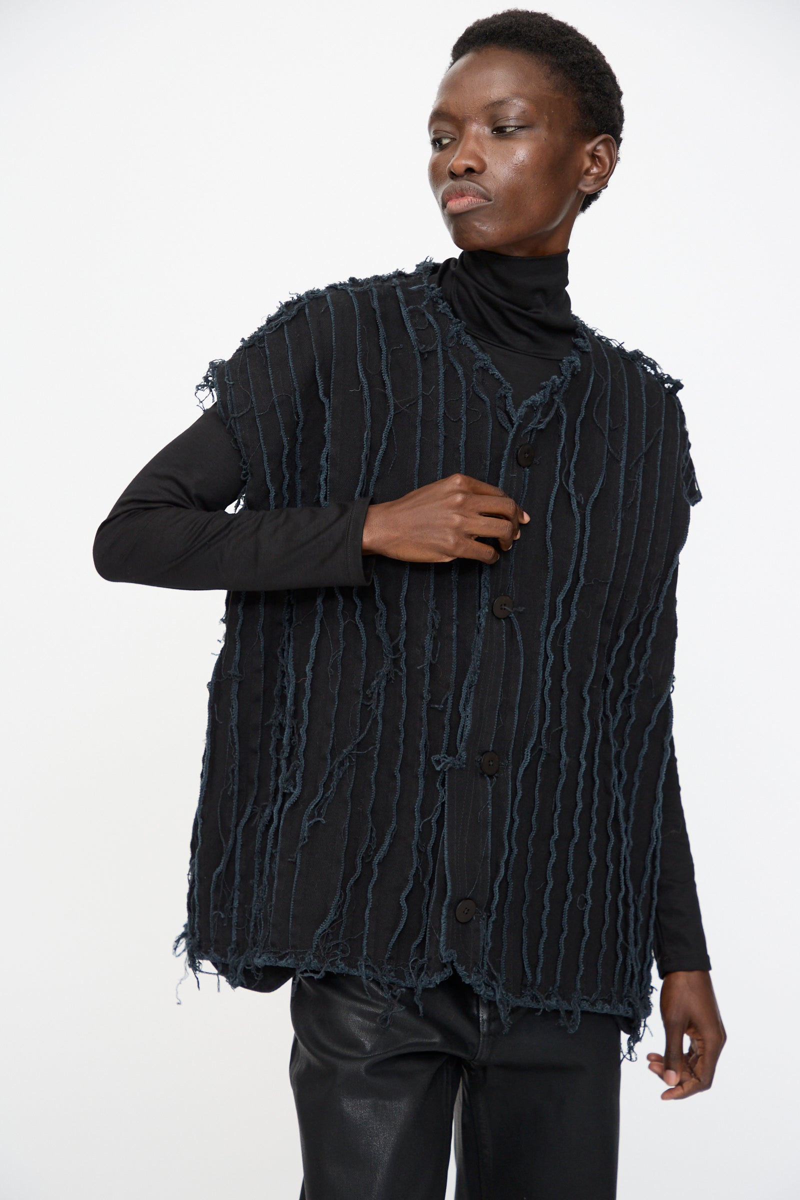 Model wears Jesse Kamm’s Deadstock 10oz. Denim Baleen Vest in Black with a black turtleneck and pants, featuring textured, fringed details, styled against a plain white background.