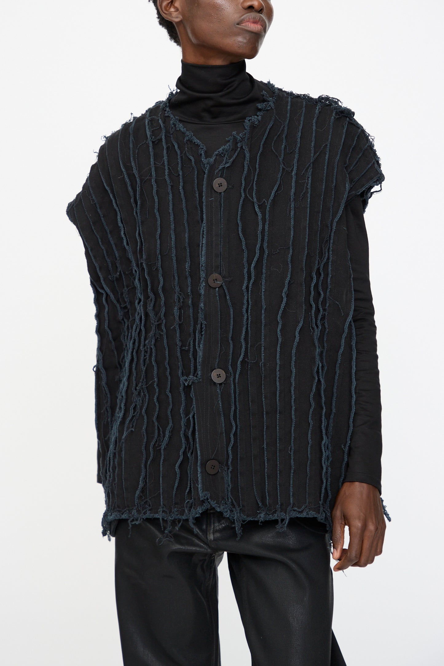 A person wearing the Jesse Kamm Deadstock 10oz. Denim Baleen Vest in Black over a black turtleneck and black pants, standing against a plain white background.