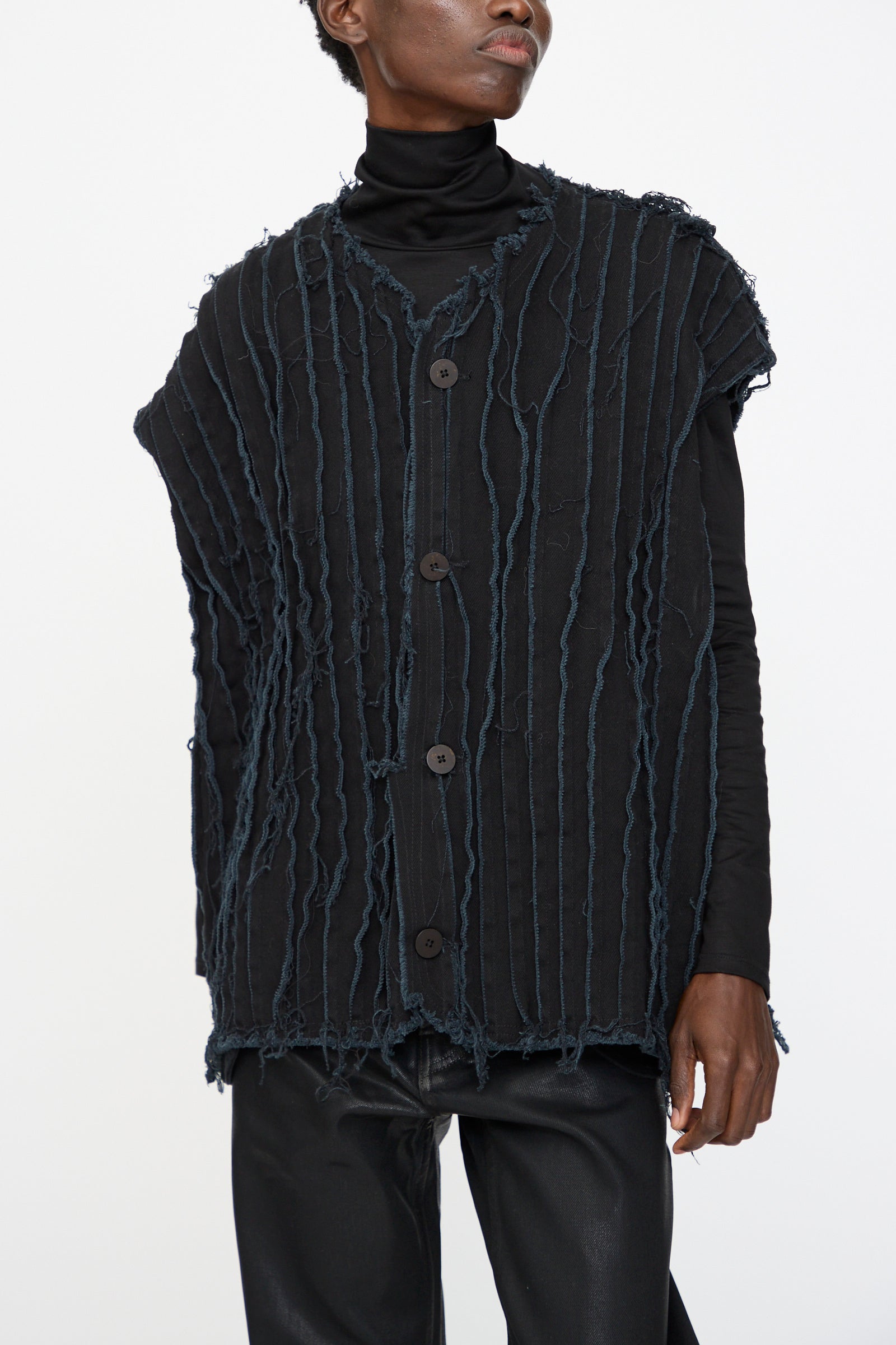 A person wearing the Jesse Kamm Deadstock 10oz. Denim Baleen Vest in Black over a black turtleneck and black pants, standing against a plain white background.