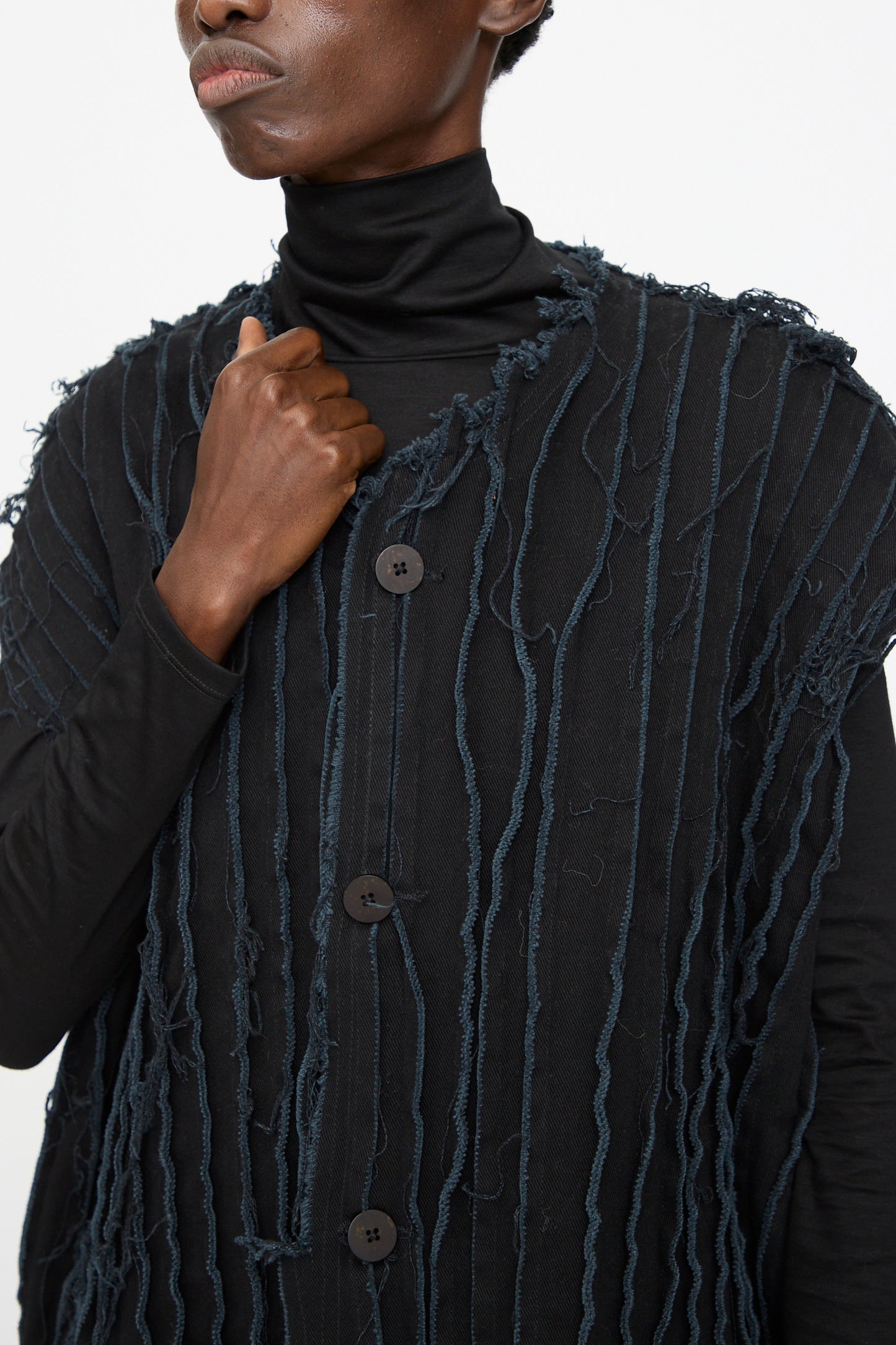 Model wears the Jesse Kamm Deadstock 10oz. Denim Baleen Vest in Black, featuring frayed vertical lines, layered over a black turtleneck. Shown from shoulders to mid-torso against a plain background.