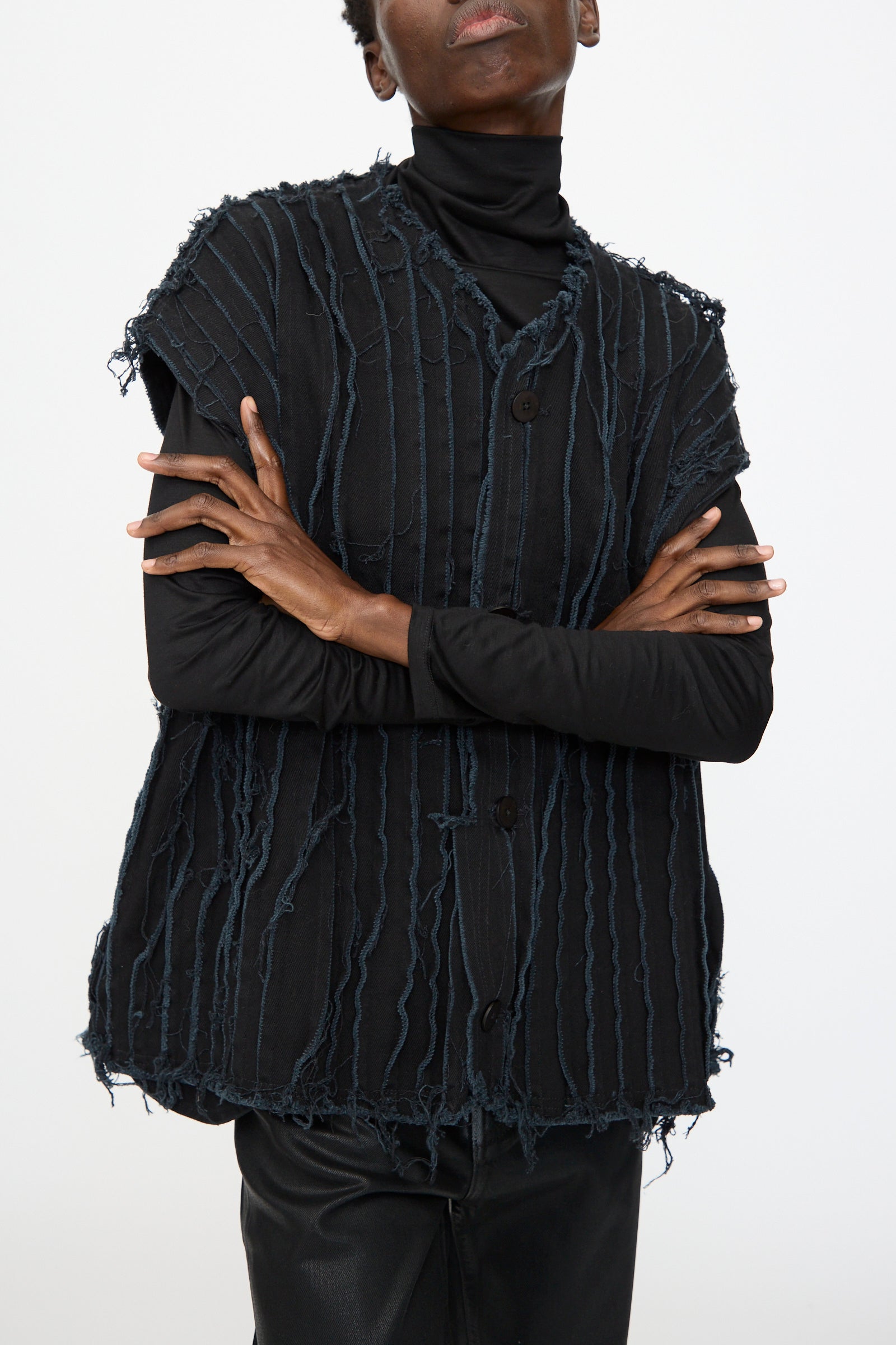 Model wears the Deadstock 10oz. Denim Baleen Vest in Black by Jesse Kamm—a textured, sleeveless, deconstructed style with frayed vertical lines—layered over a black turtleneck and black pants, arms crossed against a plain background.