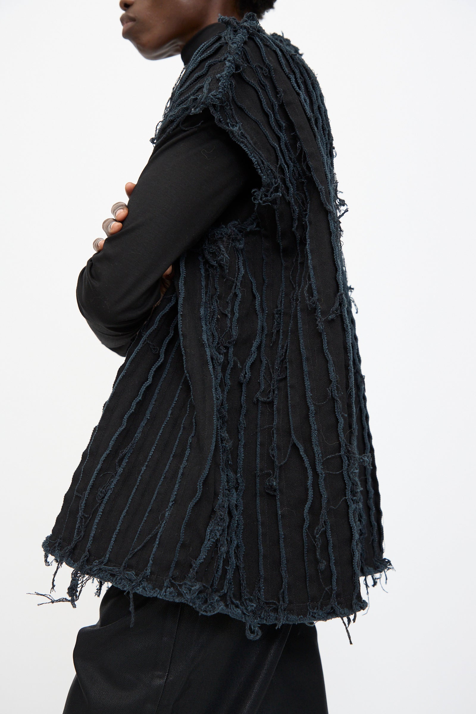 A person models the Jesse Kamm Deadstock 10oz. Denim Baleen Vest in Black, featuring deconstructed vertical frayed strips, standing with arms crossed against a plain background.