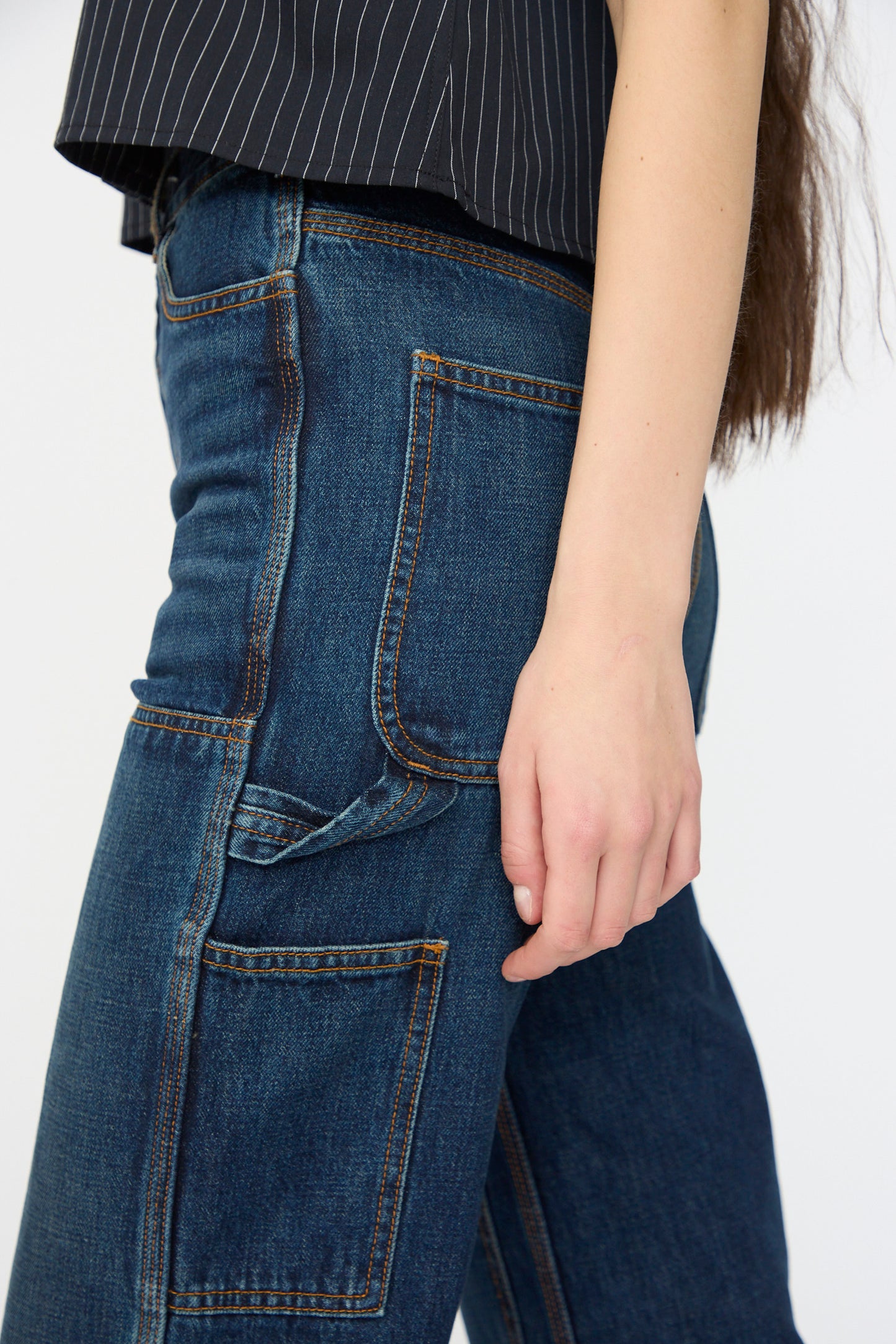 A person wears Jesse Kamm’s Denim Patchwork Handy Pants in Medium Roast, shown waist to knee, styled with a pinstripe black top and large front pockets, standing against a plain background.