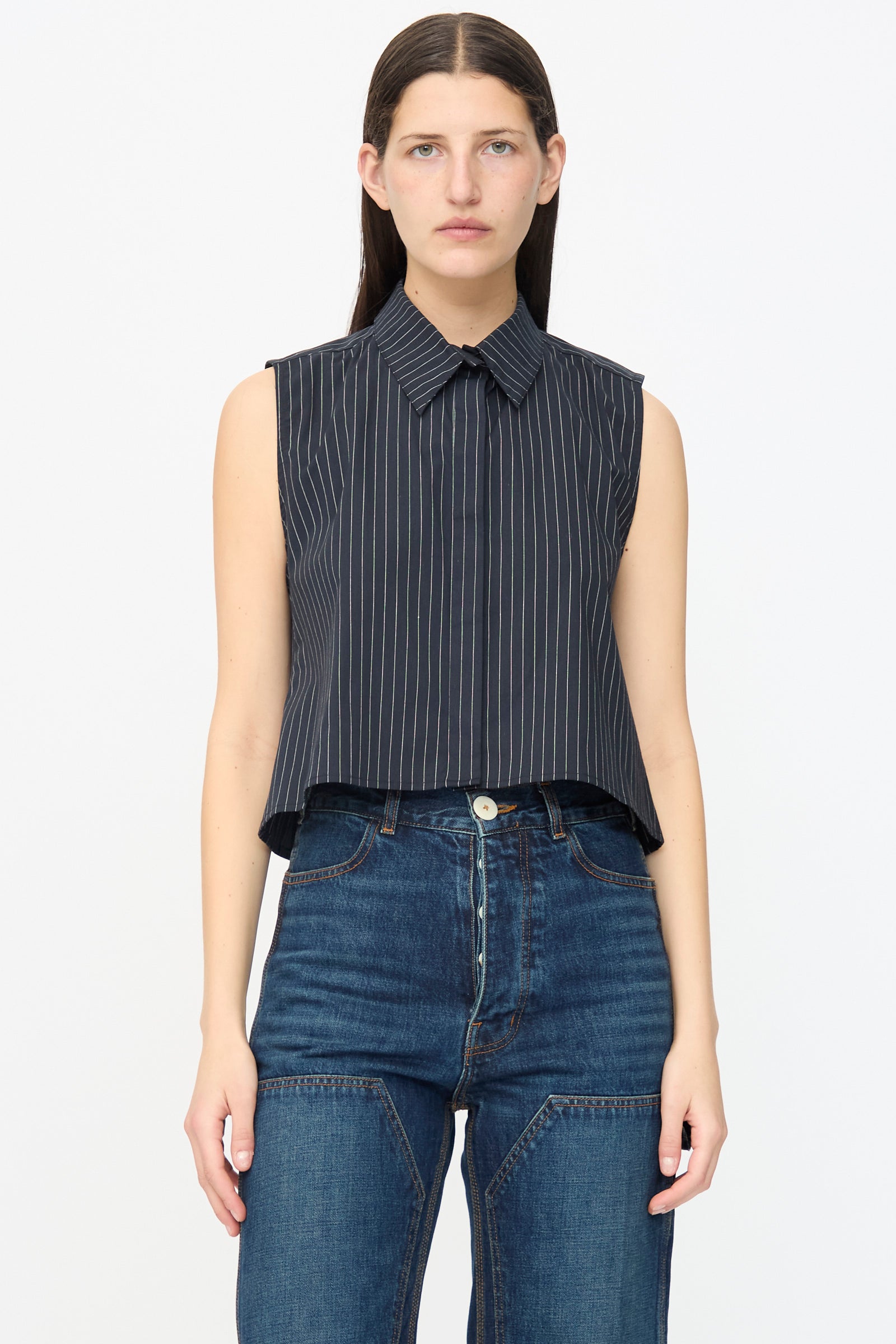 A person wears the Jesse Kamm Ellis Top in Black with Fine Ivory Stripe, paired with high-waisted blue jeans, standing against a plain white background.