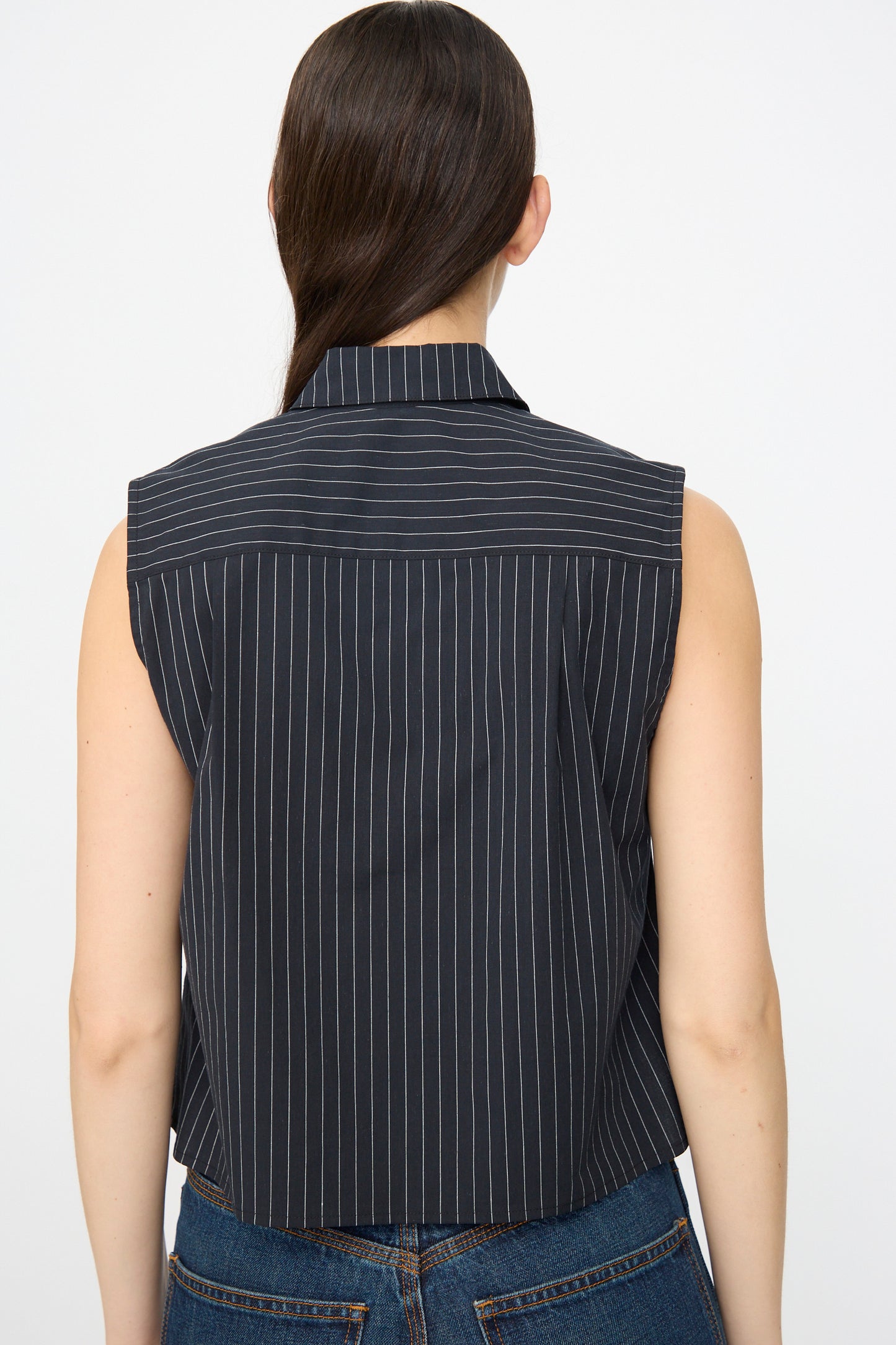 A woman with long brown hair is seen from the back wearing the Jesse Kamm Ellis Top in Black with Fine Ivory Stripe and blue jeans, posed against a plain background.