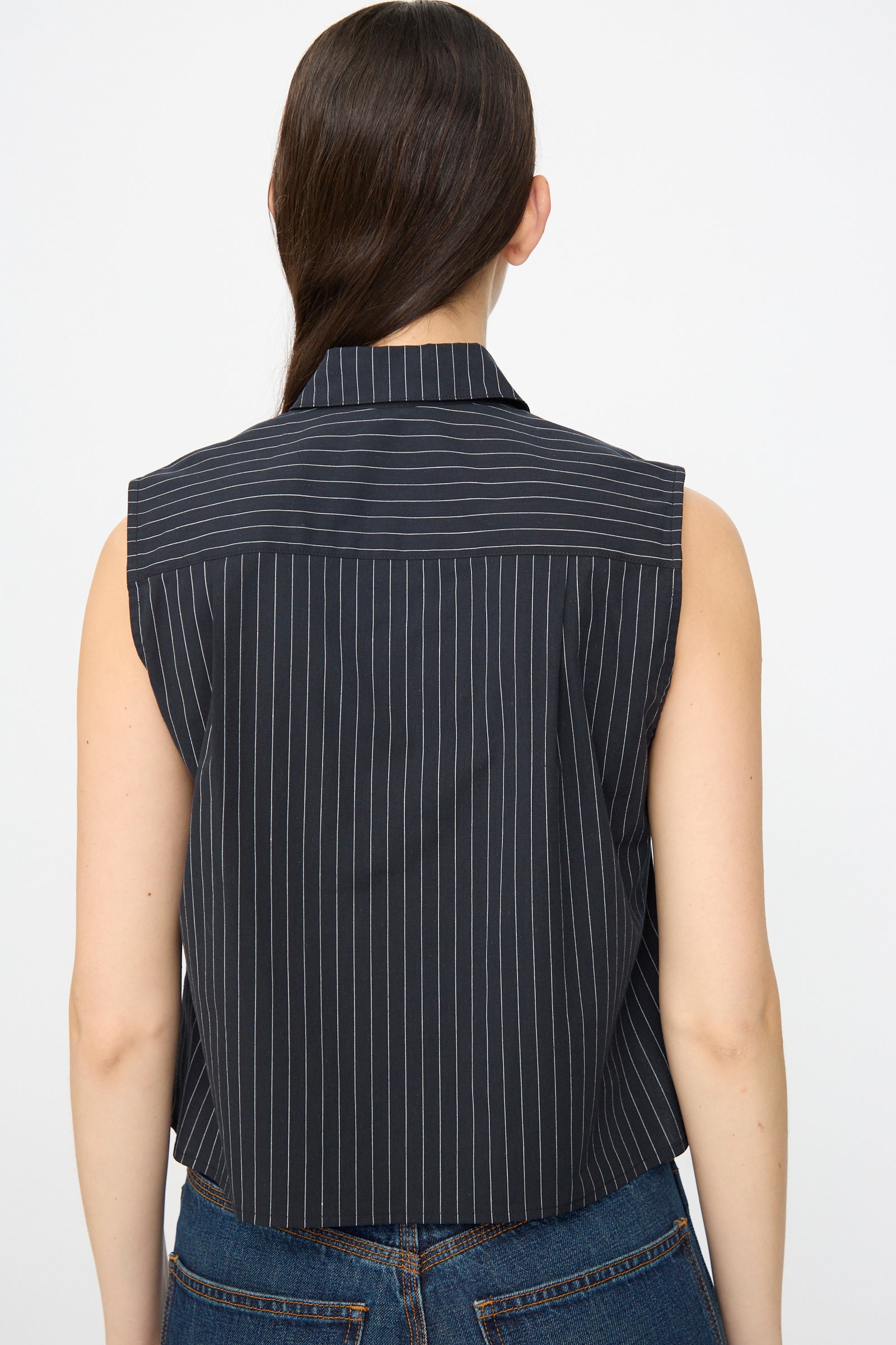 A woman with long brown hair is seen from the back wearing the Jesse Kamm Ellis Top in Black with Fine Ivory Stripe and blue jeans, posed against a plain background.