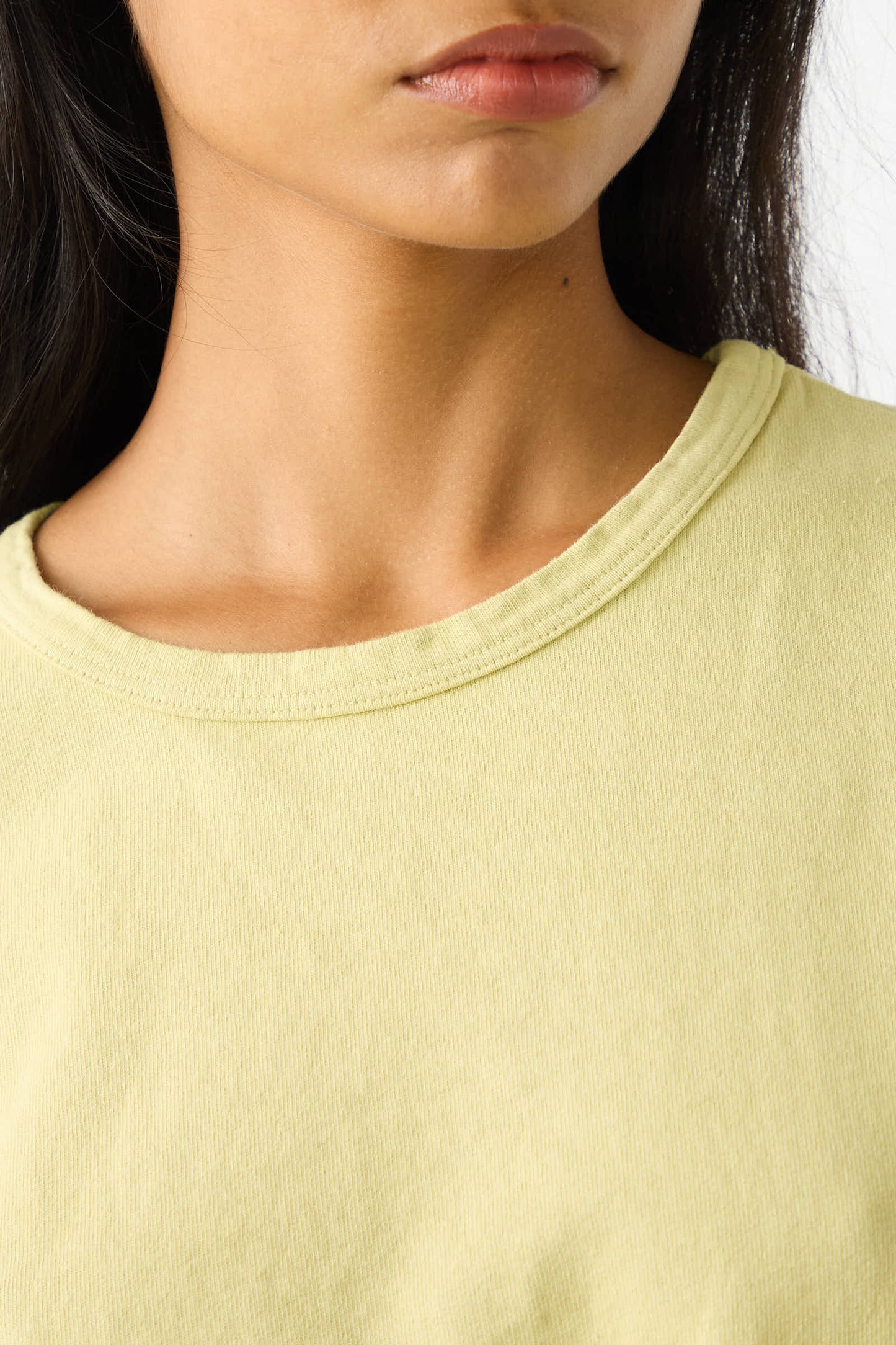 Close-up of a person wearing the Fine Cotton Knit Sailor Tee in Citroen by Jesse Kamm. The light yellow, relaxed fit crew neck shirt, made from fine knit cotton material, highlights the person's lower face and neck.