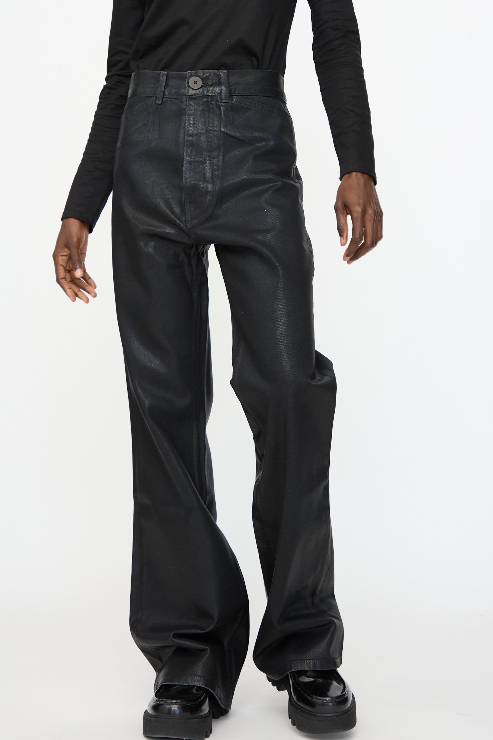 A person wearing Jesse Kamm Japanese Denim Les Deux Pants in Black Lacquer with a long-sleeve black shirt, standing against a plain white background.