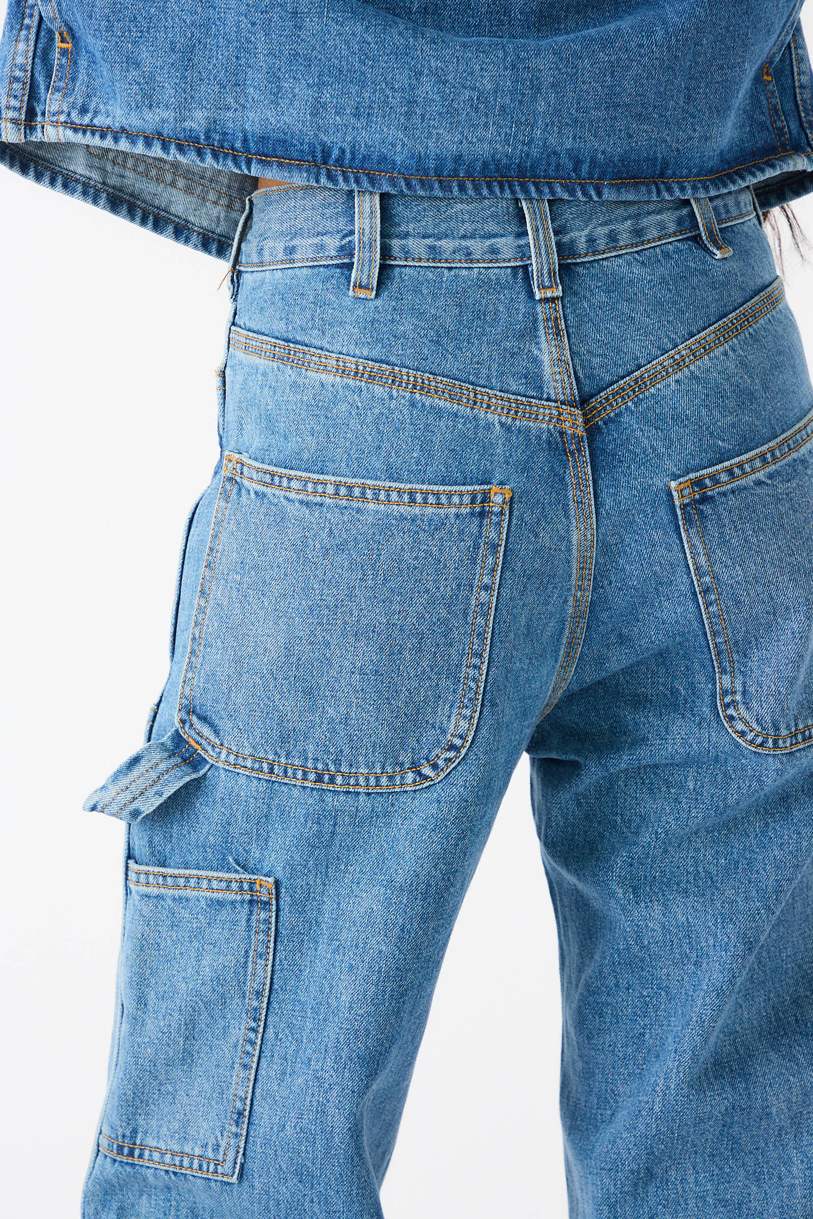 Close-up of a person wearing Japanese Denim Patchfront Handy Pant in Cowboy Blue by Jesse Kamm, featuring large back pockets and a side utility pocket, paired with a matching denim jacket.