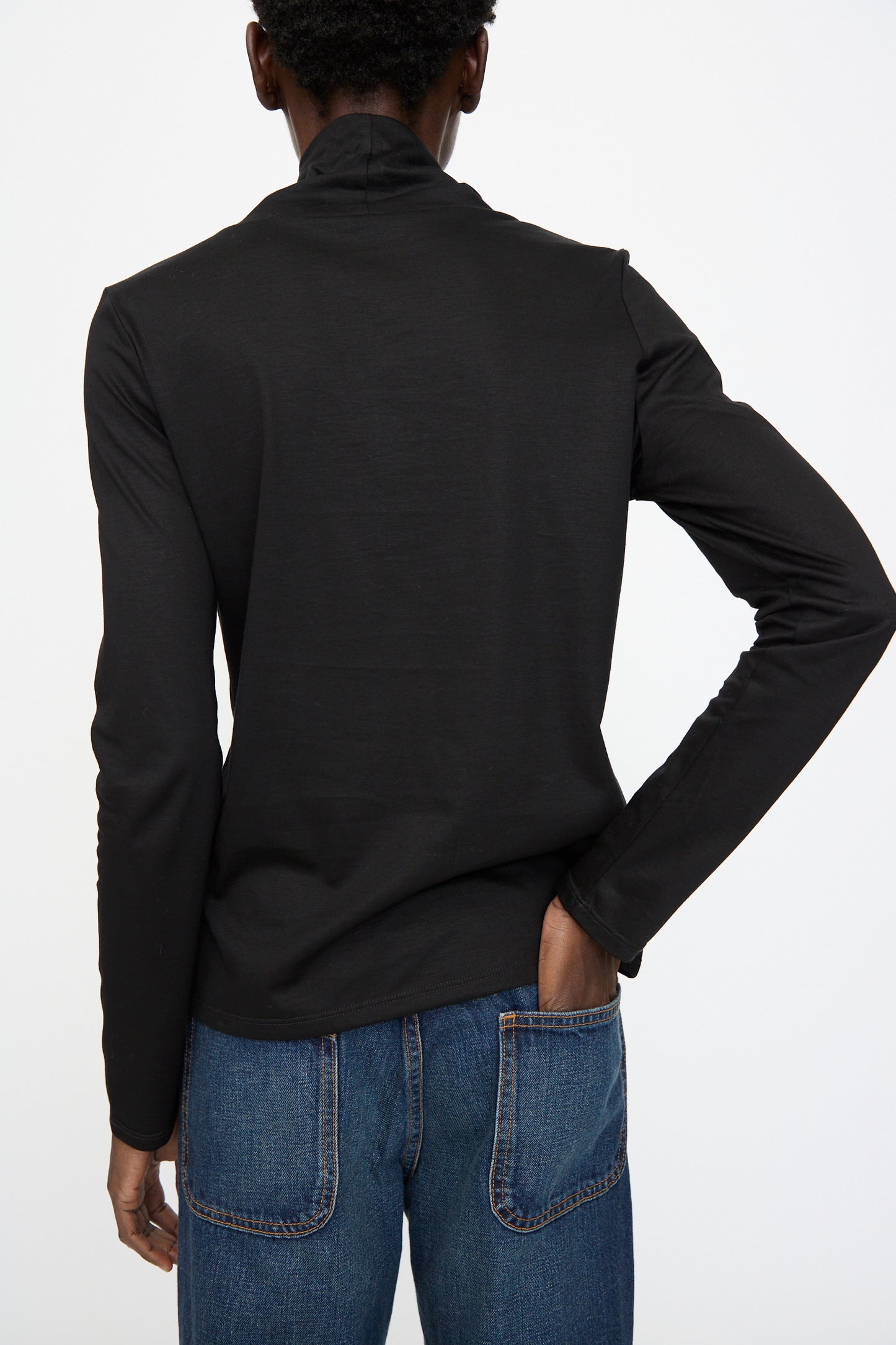 A person faces away from the camera, wearing Jesse Kamm’s Japanese Organic Cotton Classic Turtleneck in Black paired with blue jeans.