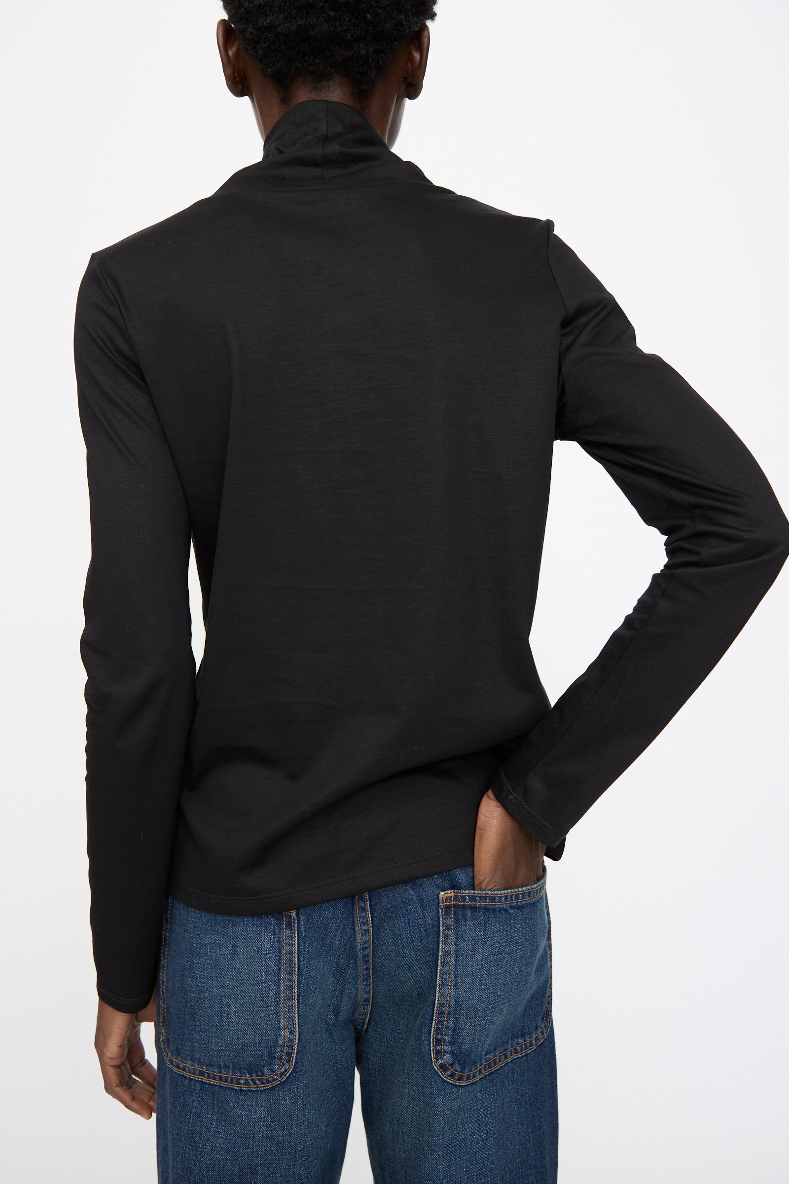 A person faces away from the camera, wearing Jesse Kamm’s Japanese Organic Cotton Classic Turtleneck in Black paired with blue jeans.