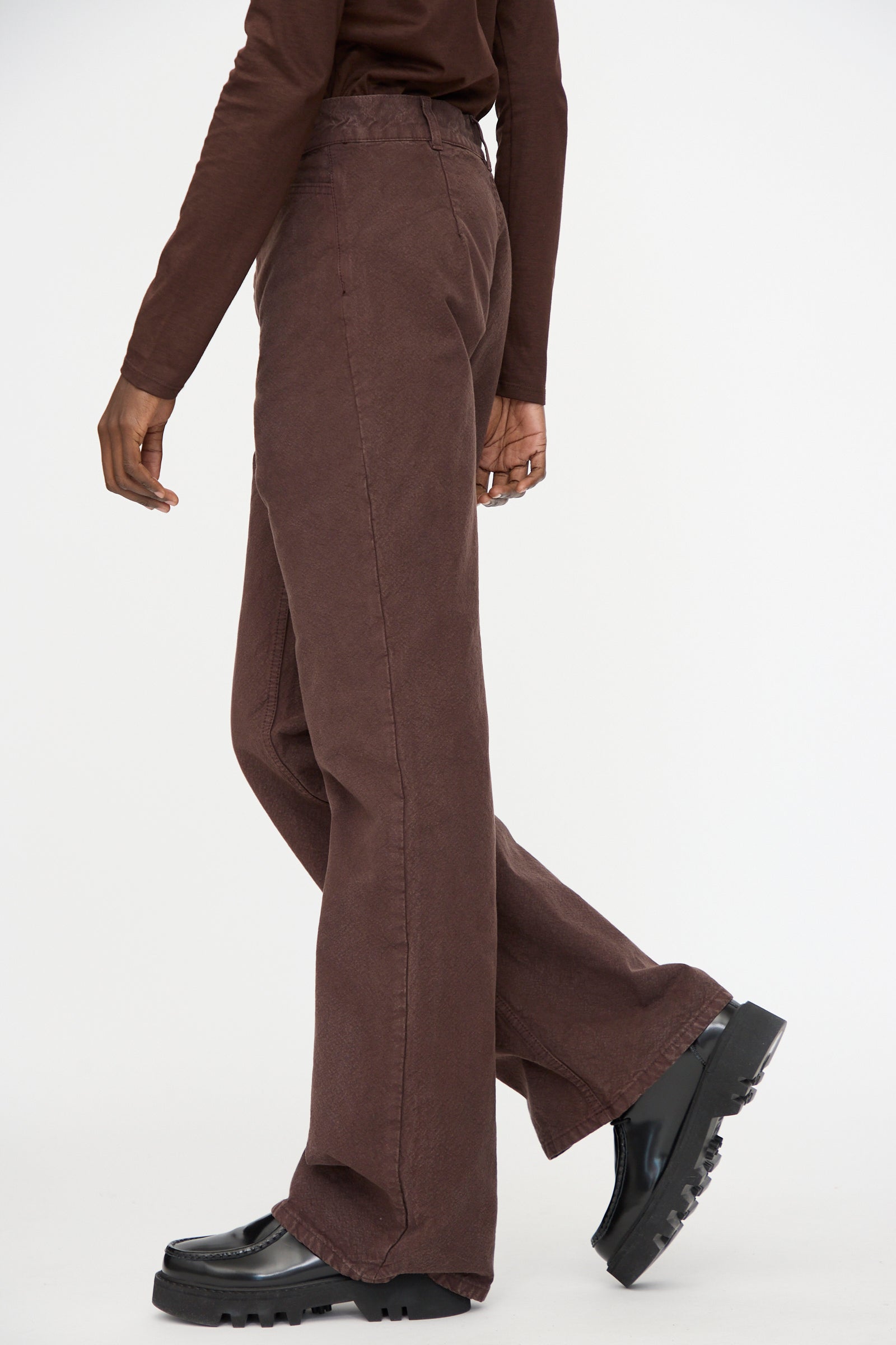 Person wearing a long-sleeve brown top, Jesse Kamm Organic Canvas Les Deux Pants in Raisin (high-waisted), and black chunky shoes, shown from the side against a plain white background.