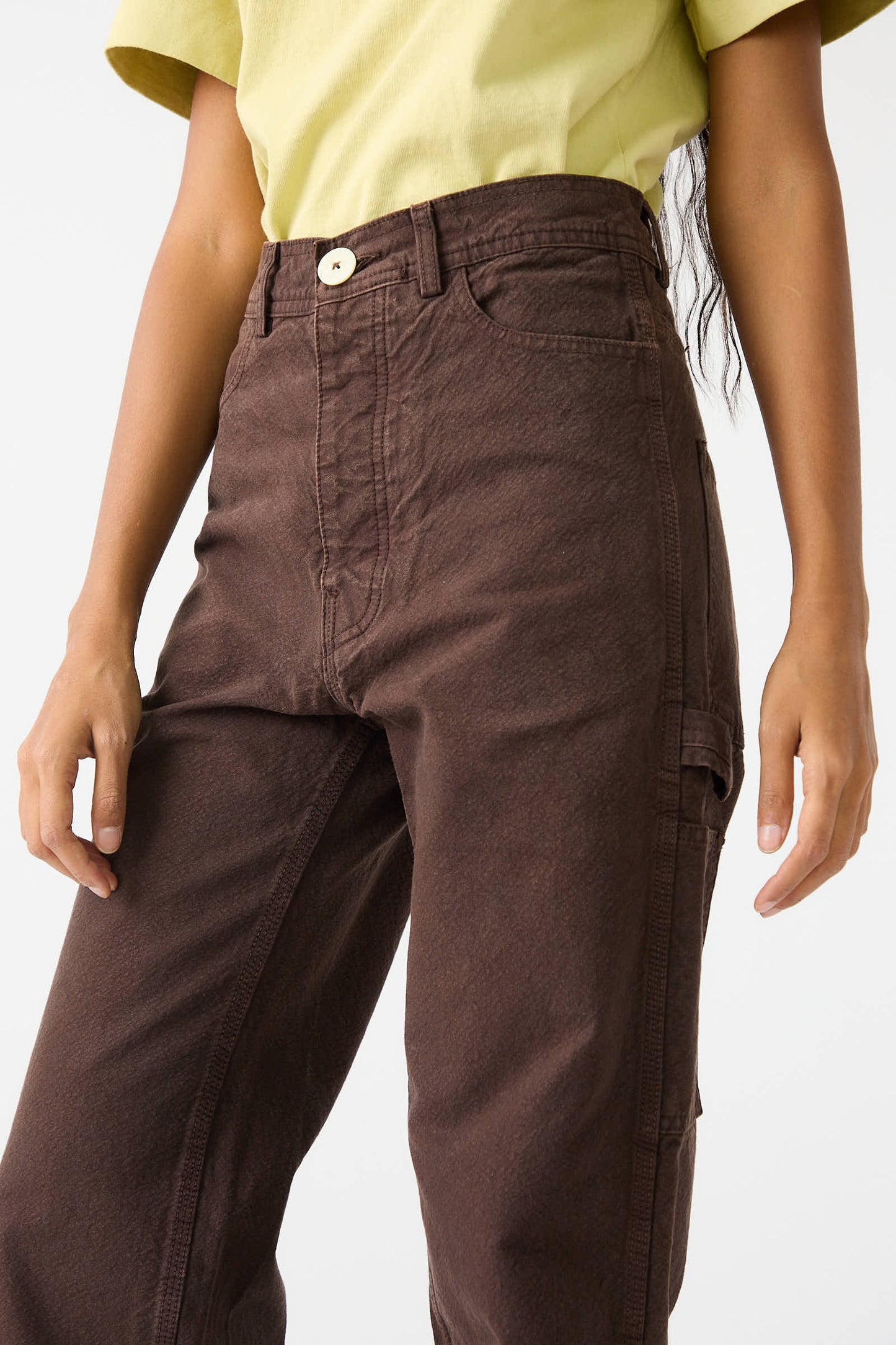 Person wearing Jesse Kamm's Organic Cotton Canvas Handy Pant in Raisin, which features a high waist with a wide-leg, relaxed fit, and a light yellow short-sleeve shirt. Only the lower half of the person's torso is visible.