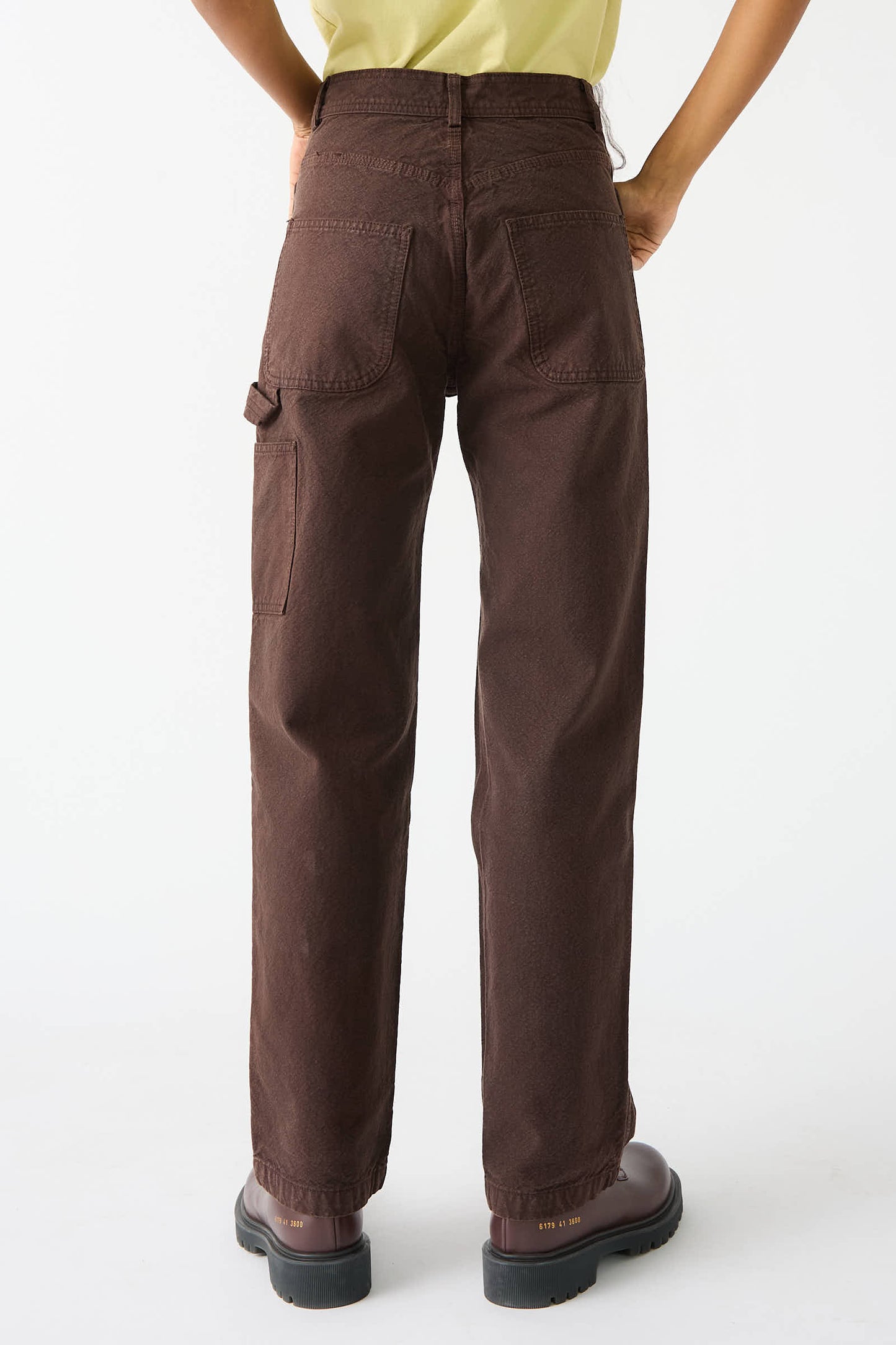 A person wearing Jesse Kamm's Organic Cotton Canvas Handy Pant in Raisin paired with brown boots, viewed from the back.