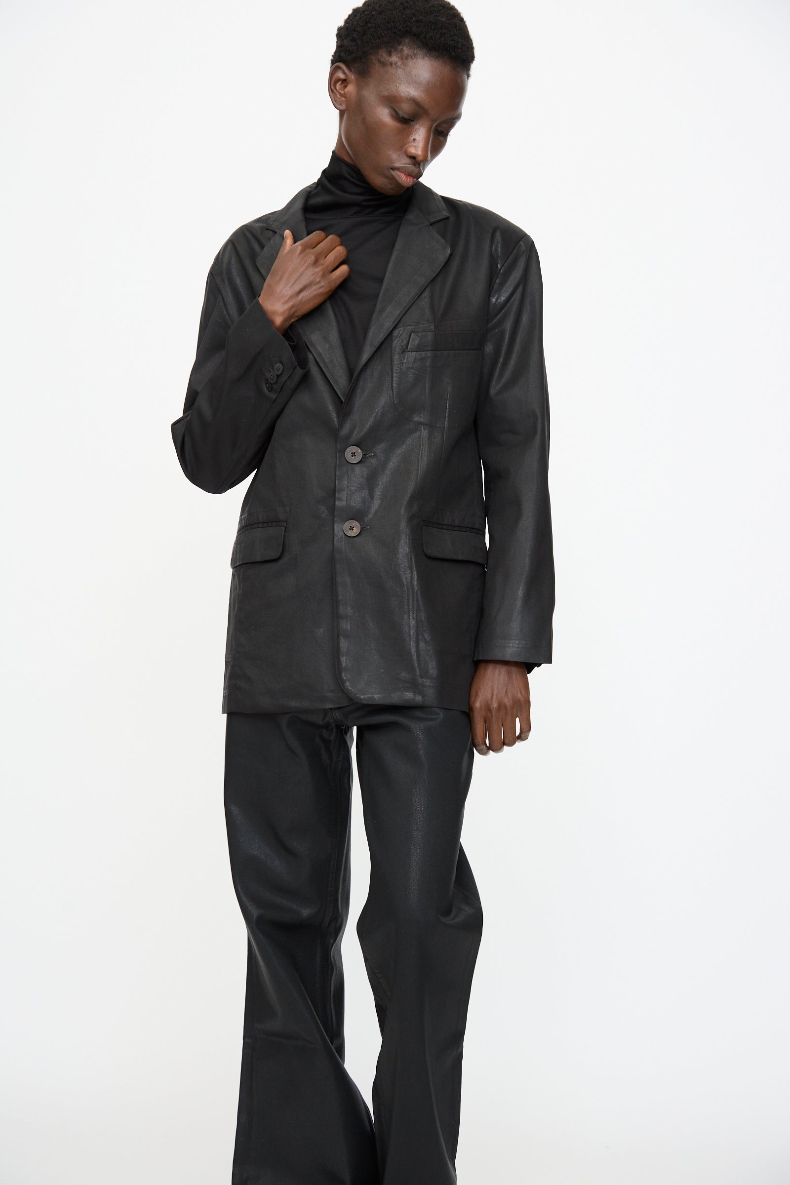 Model wears the Jesse Kamm Organic Twill Fianna Blazer in Black Lacquer over a black turtleneck and black leather pants, standing against a plain white background.
