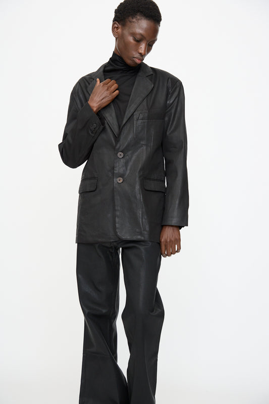 Model wears the Jesse Kamm Organic Twill Fianna Blazer in Black Lacquer over a black turtleneck and black leather pants, standing against a plain white background.