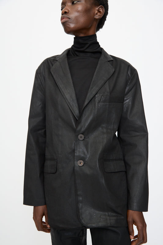 Model wears the Jesse Kamm Organic Twill Fianna Blazer in Black Lacquer and a black turtleneck, posed against a plain white background.