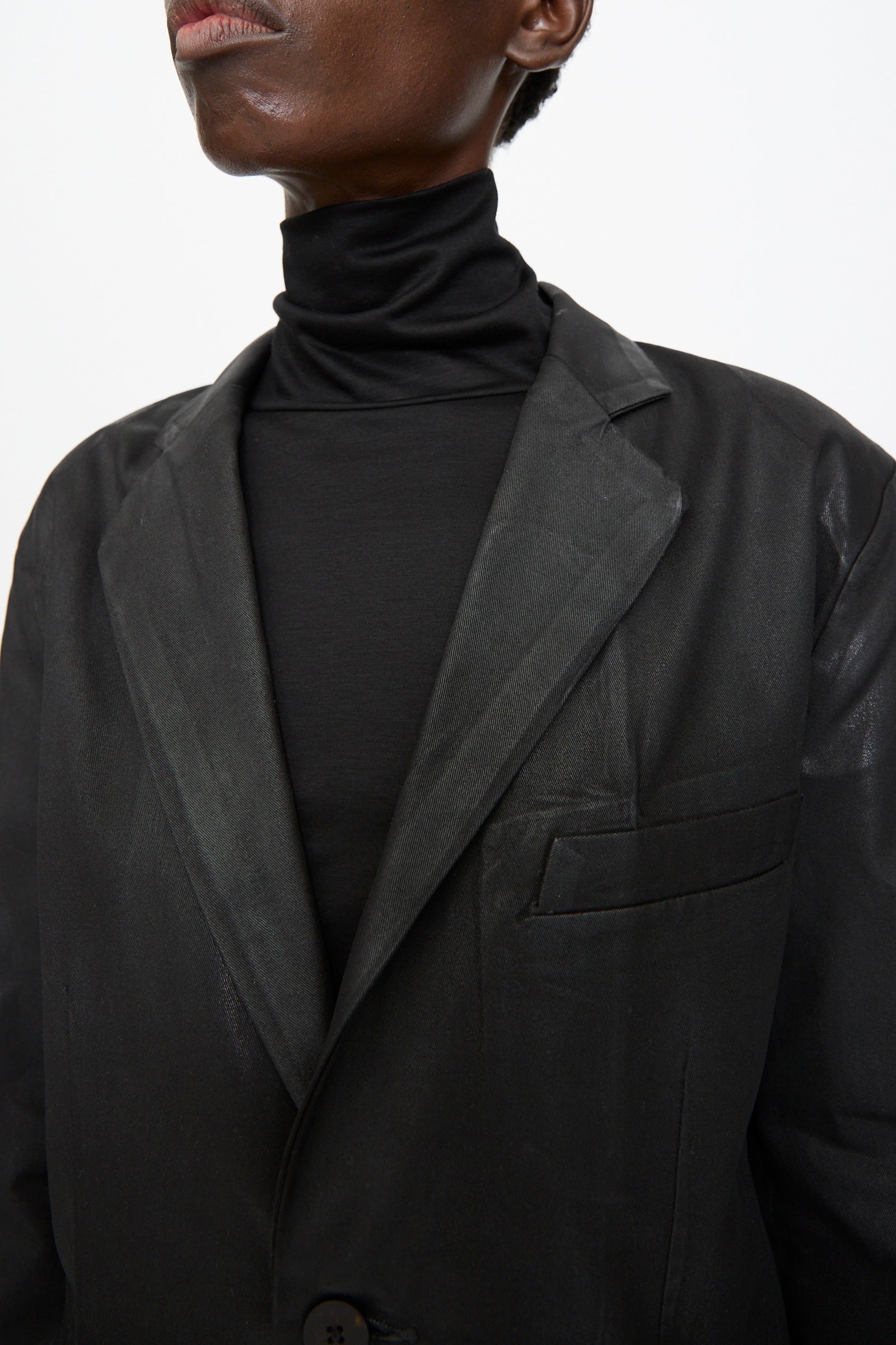 Model shown from the shoulders up against a plain background, wearing Jesse Kamm’s Organic Twill Fianna Blazer in Black Lacquer over a black turtleneck.