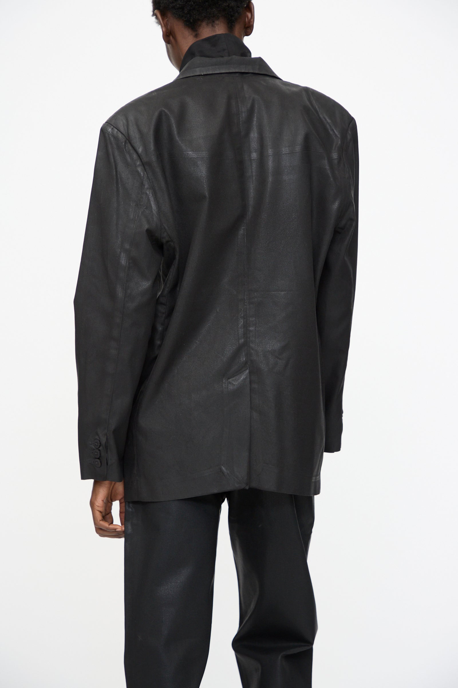 A person wearing the Jesse Kamm Organic Twill Fianna Blazer in Black Lacquer and black pants faces away from the camera against a plain white background.