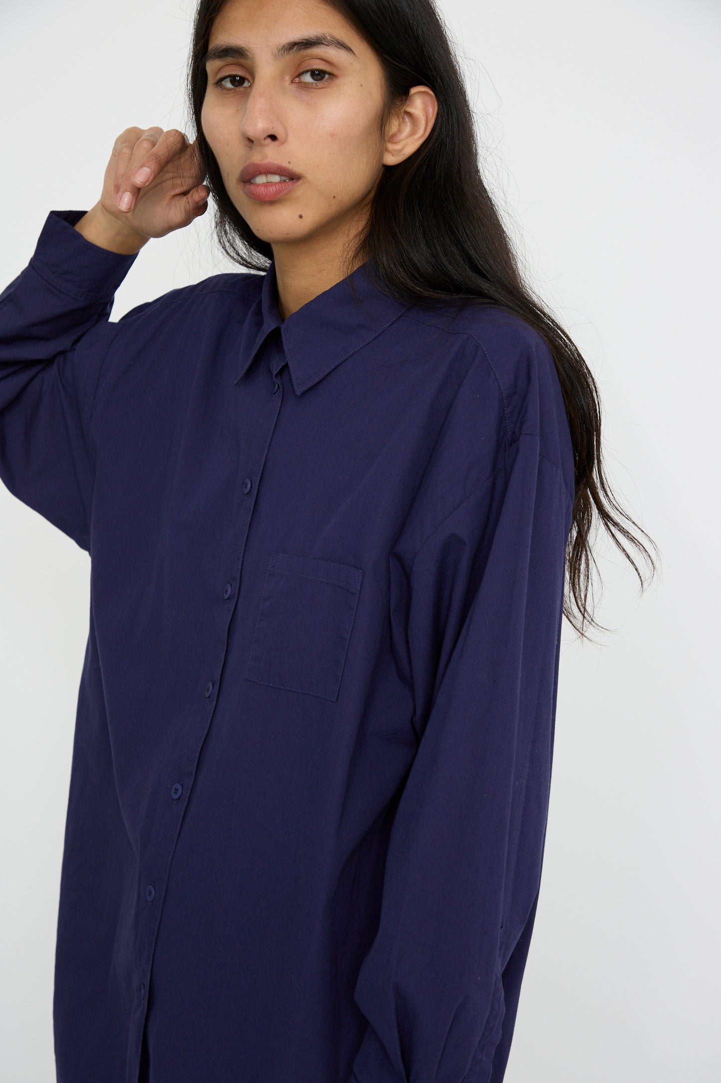 A person with long dark hair is wearing a Painter Shirt in Bill Cunningham Blue by Jesse Kamm, crafted from soft cotton poplin, against a white background.