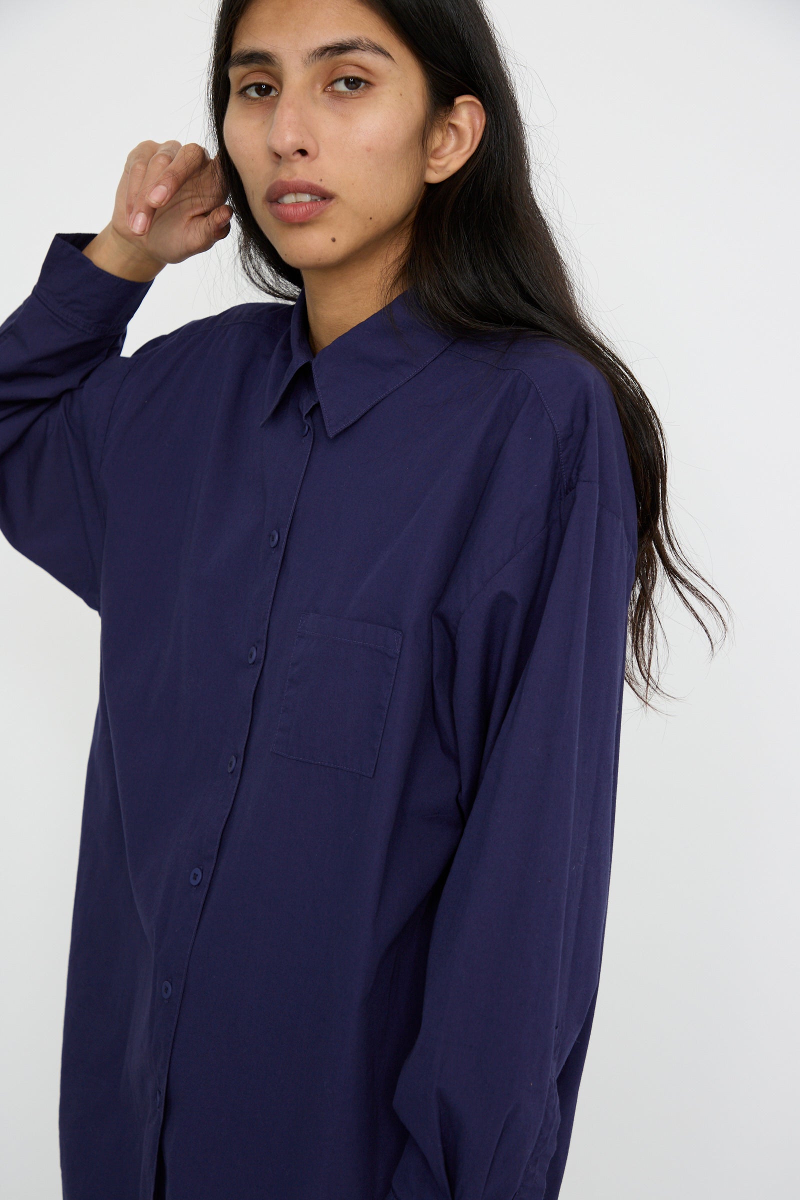 A person with long dark hair is wearing a Painter Shirt in Bill Cunningham Blue by Jesse Kamm, crafted from soft cotton poplin, against a white background.