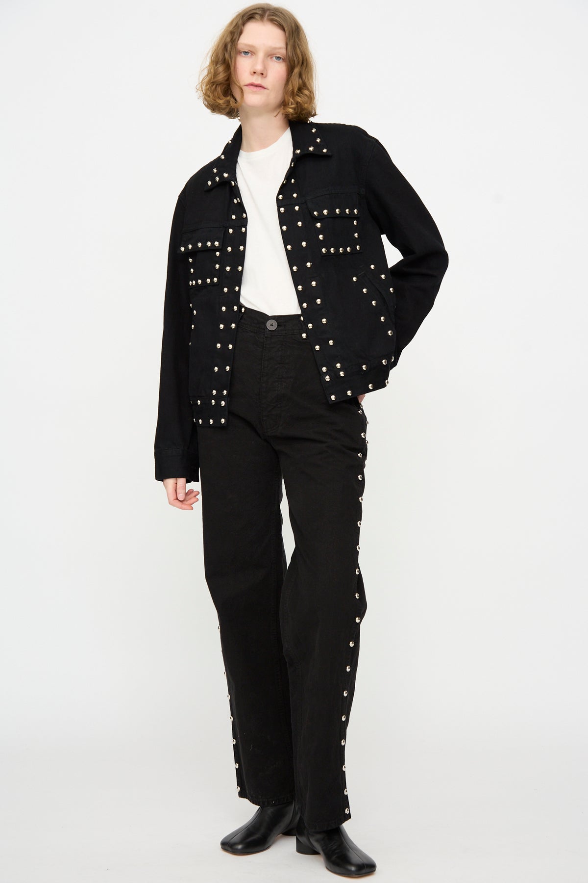 A model wears the Jesse Kamm Ranch Jacket in Black Overdye with Studs, paired with matching pants, a white shirt, and black boots, standing against a plain white background.