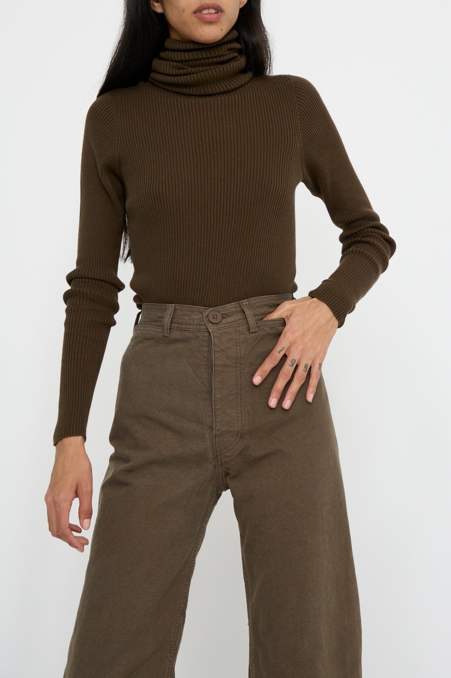 A person wearing a brown turtleneck sweater and matching Jesse Kamm's Sailor Pant in Mushroom stands against a plain background.