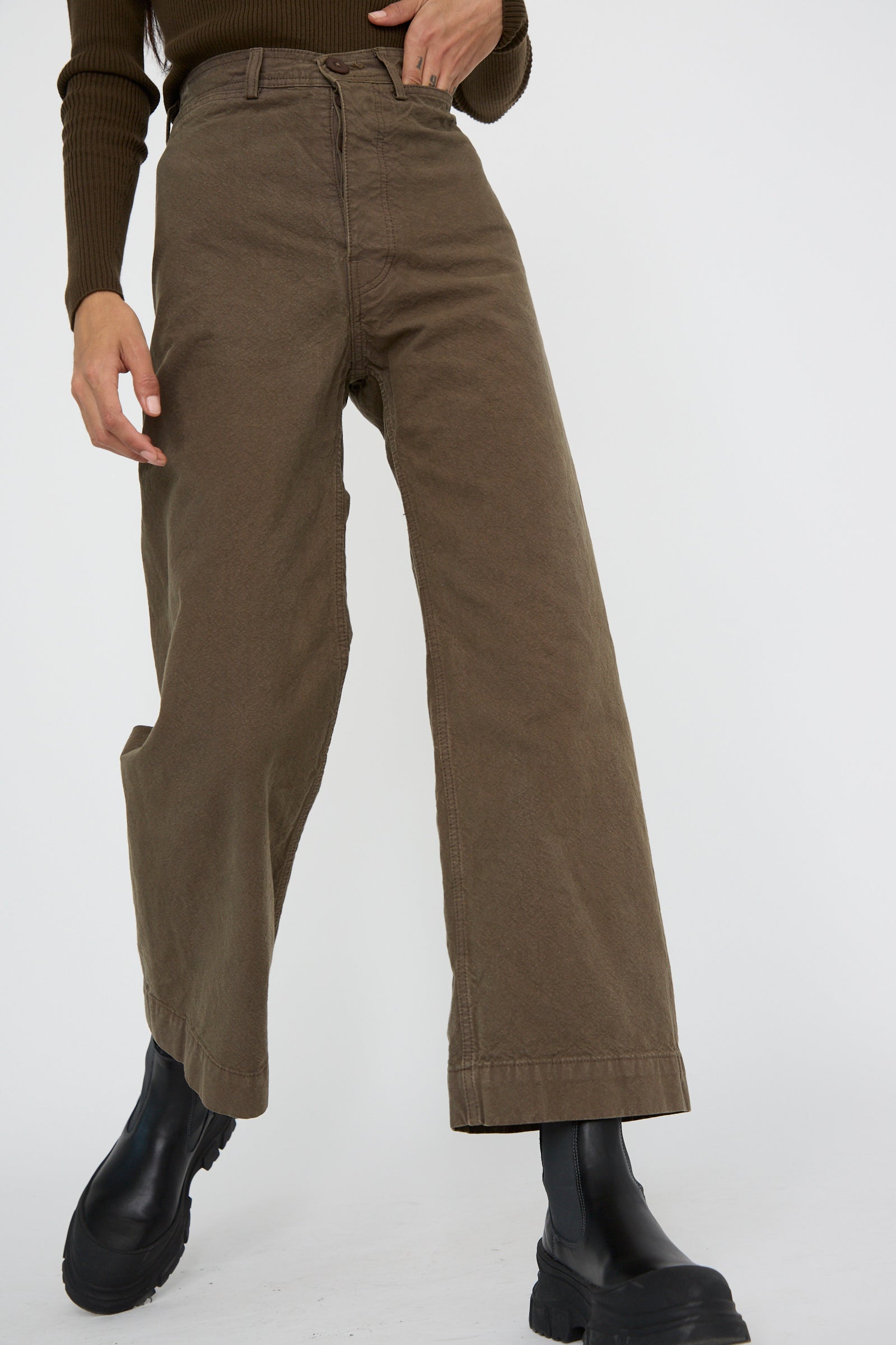 A person from below the waist wearing the Jesse Kamm Sailor Pant in Mushroom paired with black boots against a plain background.