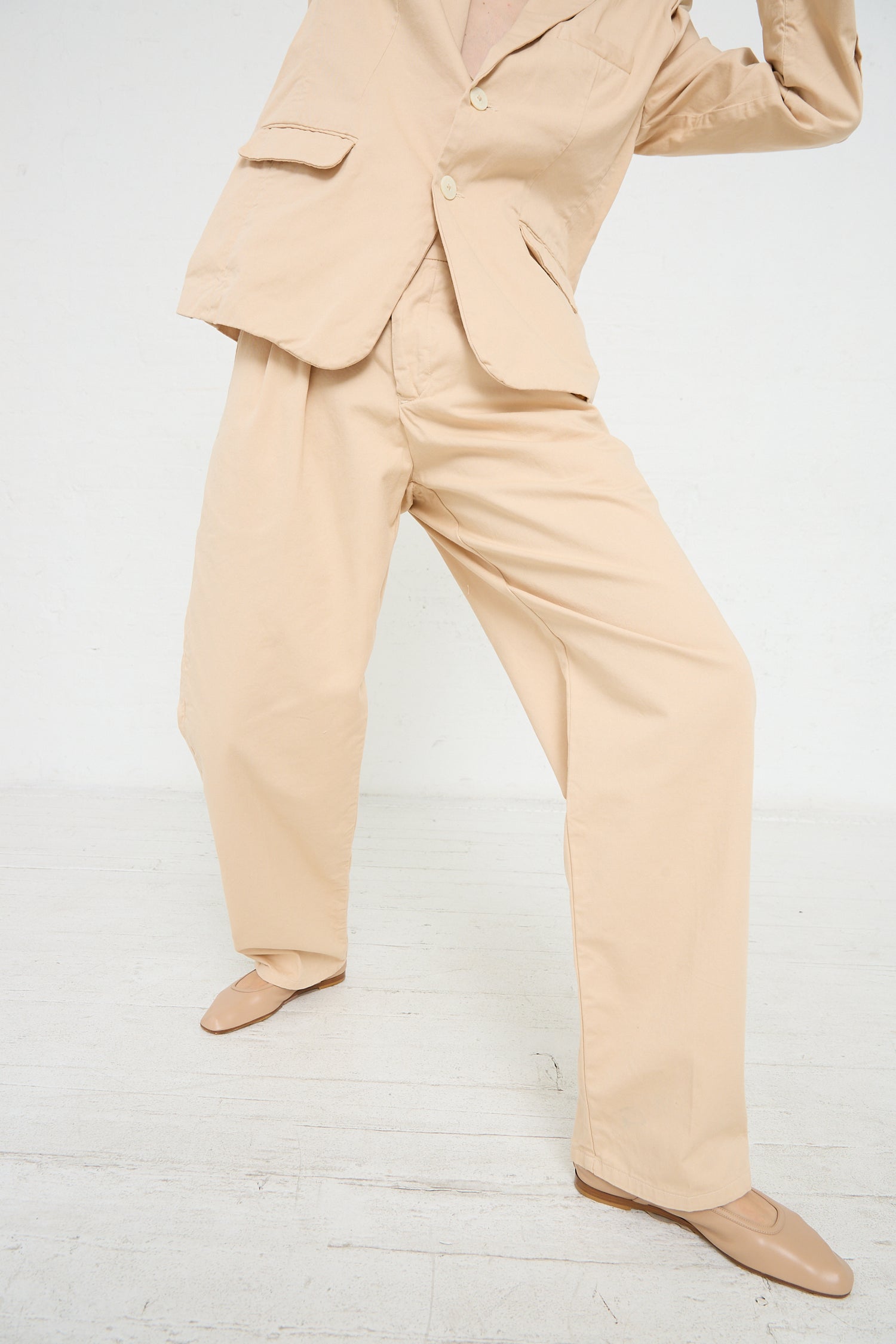 A woman in a tan suit is posing in front of a white wall, showcasing her Jesse Kamm Trouser in Buff.