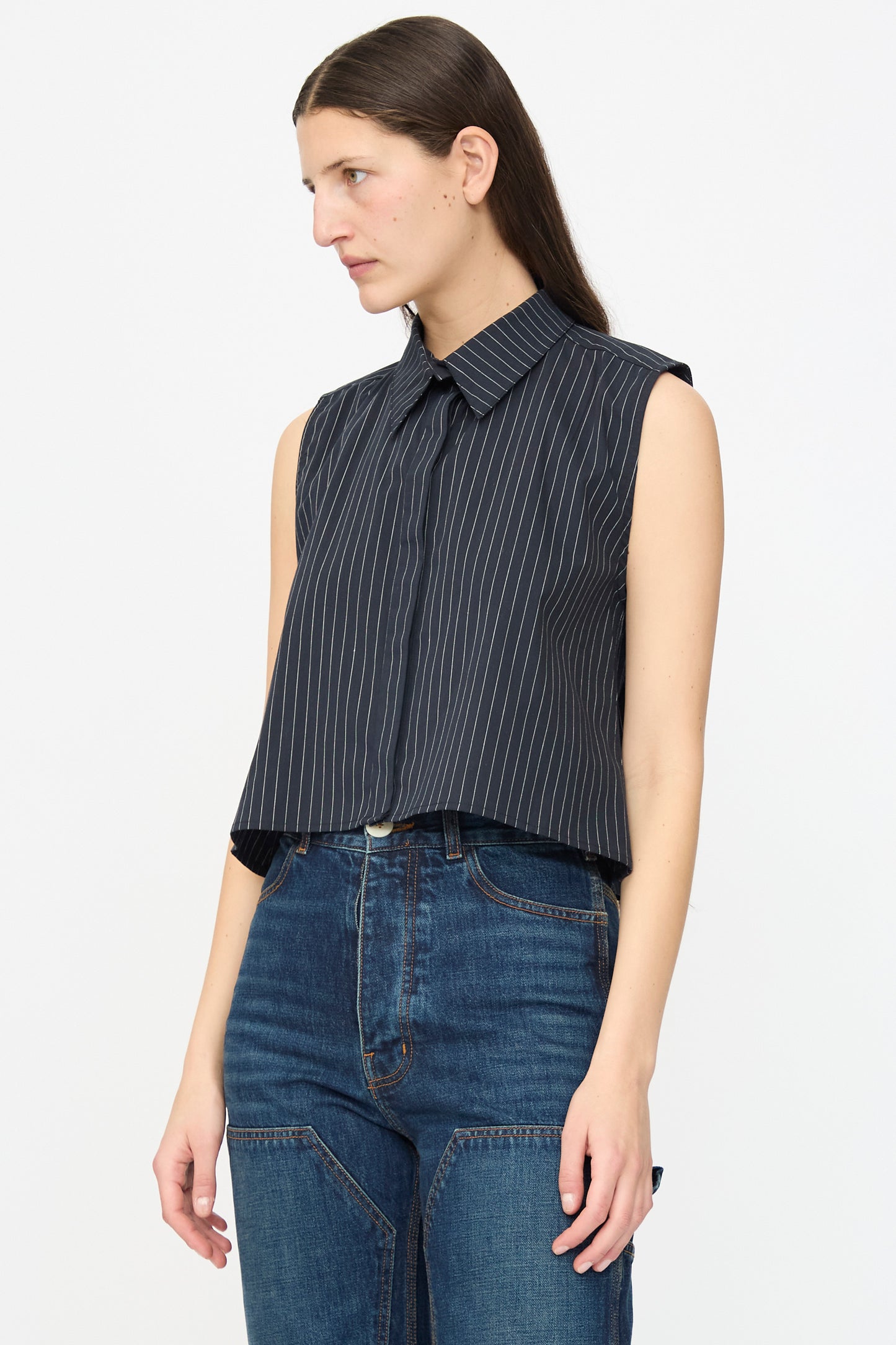 A person wearing the Ellis Top in Black with Fine Ivory Stripe by Jesse Kamm and high-waisted blue jeans stands against a plain white background.