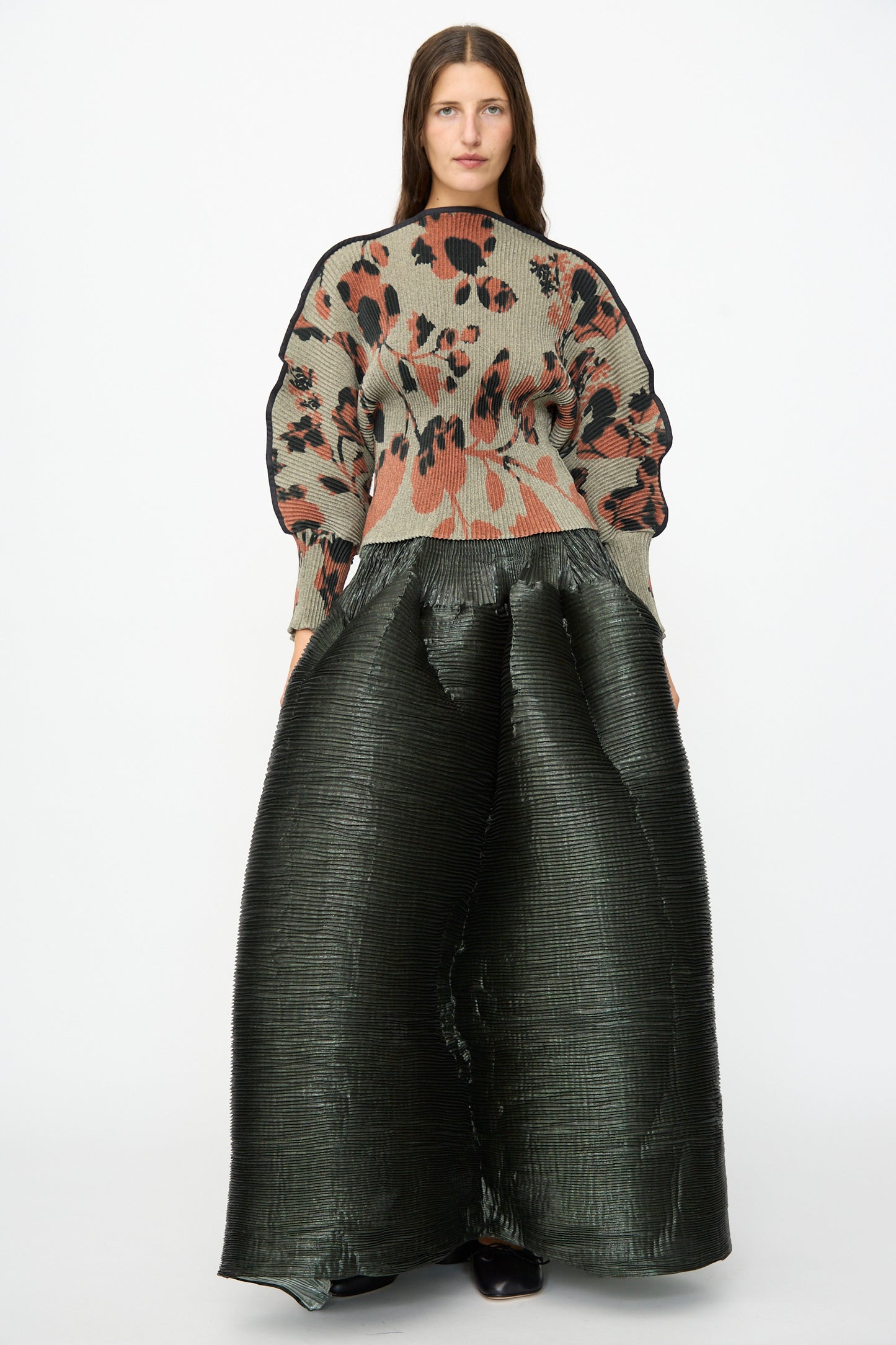 A person stands facing forward against a plain white background, wearing a patterned oversized sweater and the Julia Heuer Kenza Handpleated Skirt in Moss Metallic.