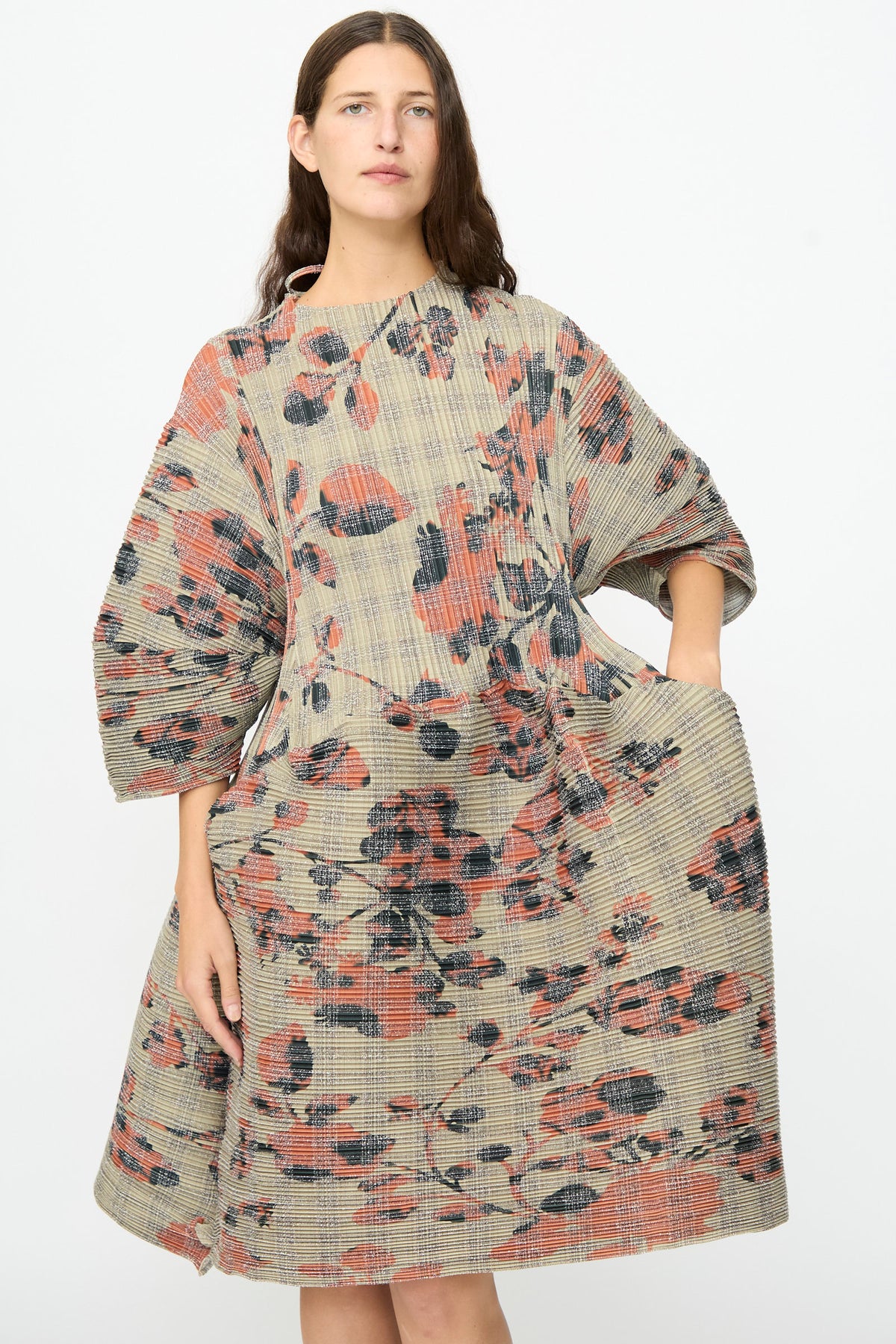 A woman wearing the Julia Heuer Pax Pleated Dress in Sandy Ingrid, a loose-fitting, sculptural midi dress with wide sleeves and an abstract floral pattern in muted red, black, and beige tones.