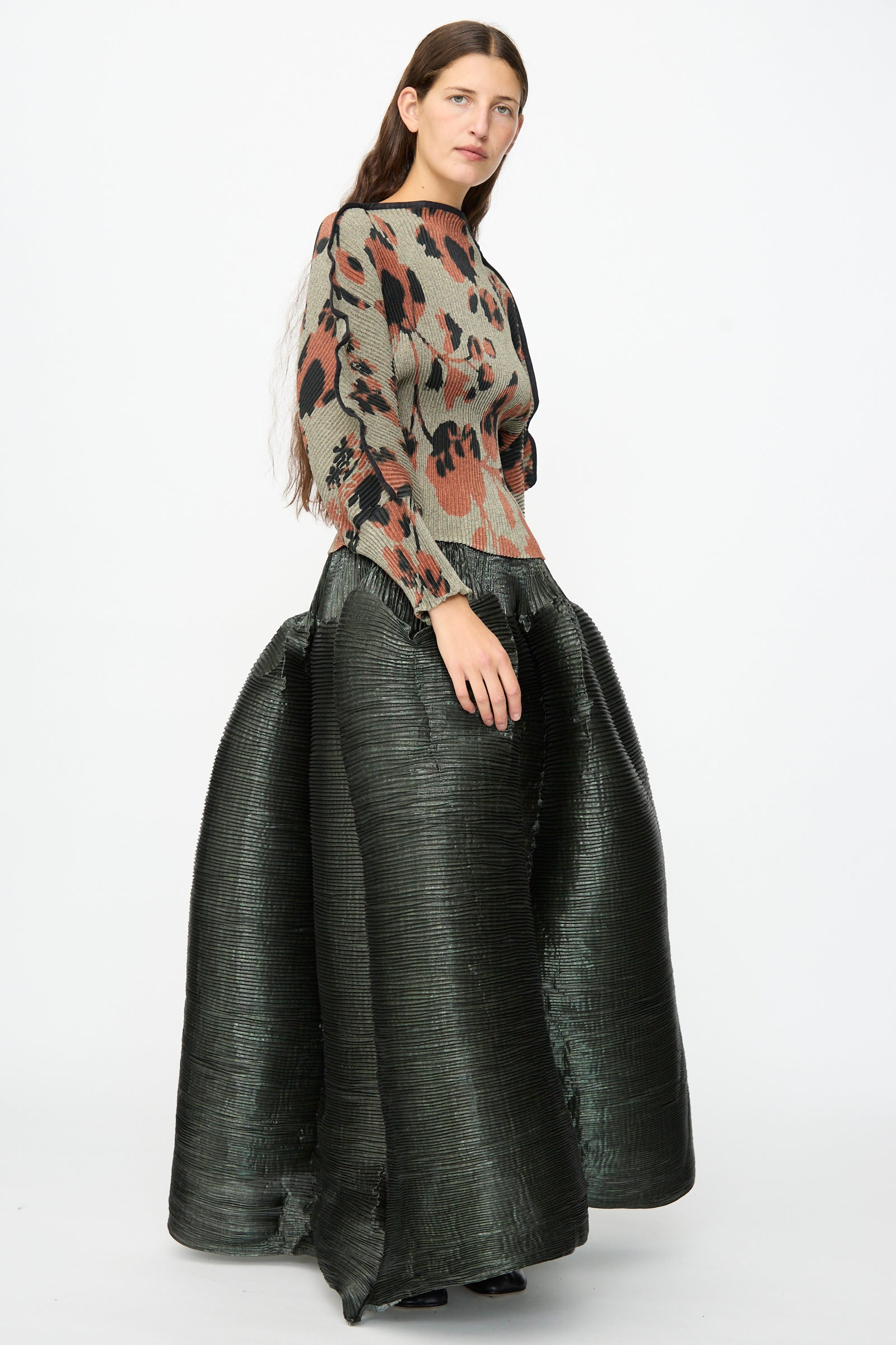 A woman wearing the Julia Heuer Radok Pleated Knit Pullover in Ingrid, paired with a voluminous, structured black skirt, stands against a plain white background. The ensemble showcases the refined elegance of French craftsmanship, echoing the timeless appeal of pieces made in France.