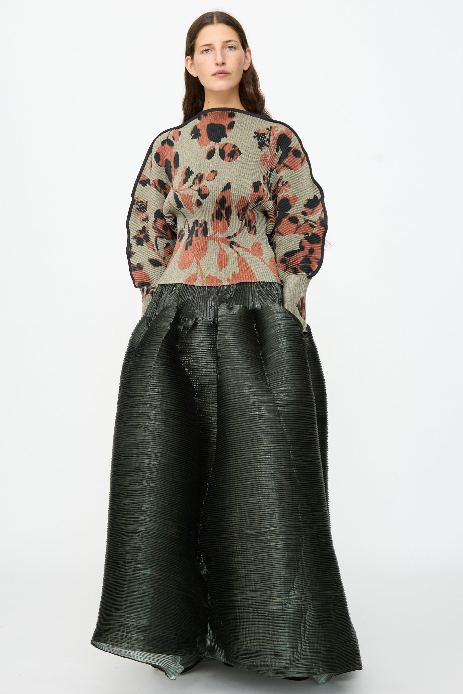 A woman stands against a plain background wearing the Julia Heuer Radok Pleated Knit Pullover in Ingrid and large, textured black wide-leg pants, each piece artfully made in France.