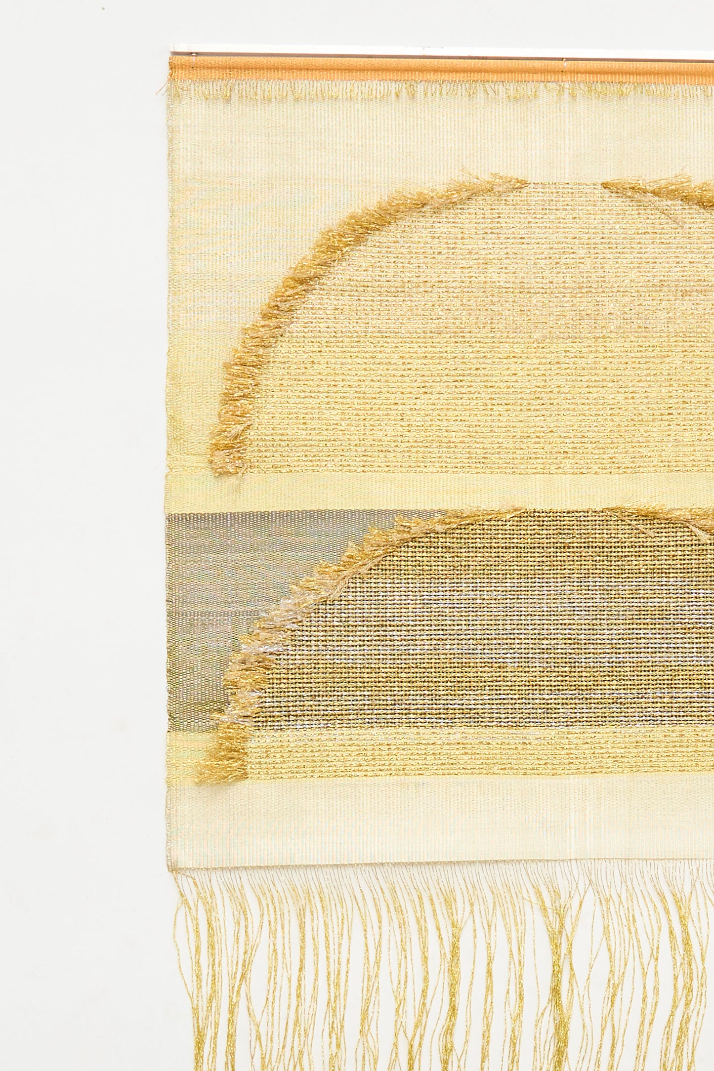 Handmade in the UK, the Two Suns Rising Weaving by Justine Ashbee is a woven rectangle wall hanging with two gold-tone semicircles, metallic fiber accents, and fringe and loose threads at the bottom.