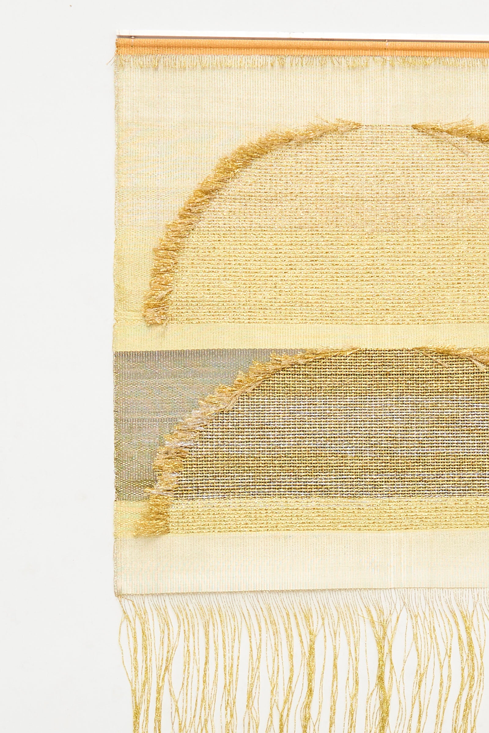 Handmade in the UK, the Two Suns Rising Weaving by Justine Ashbee is a woven rectangle wall hanging with two gold-tone semicircles, metallic fiber accents, and fringe and loose threads at the bottom.