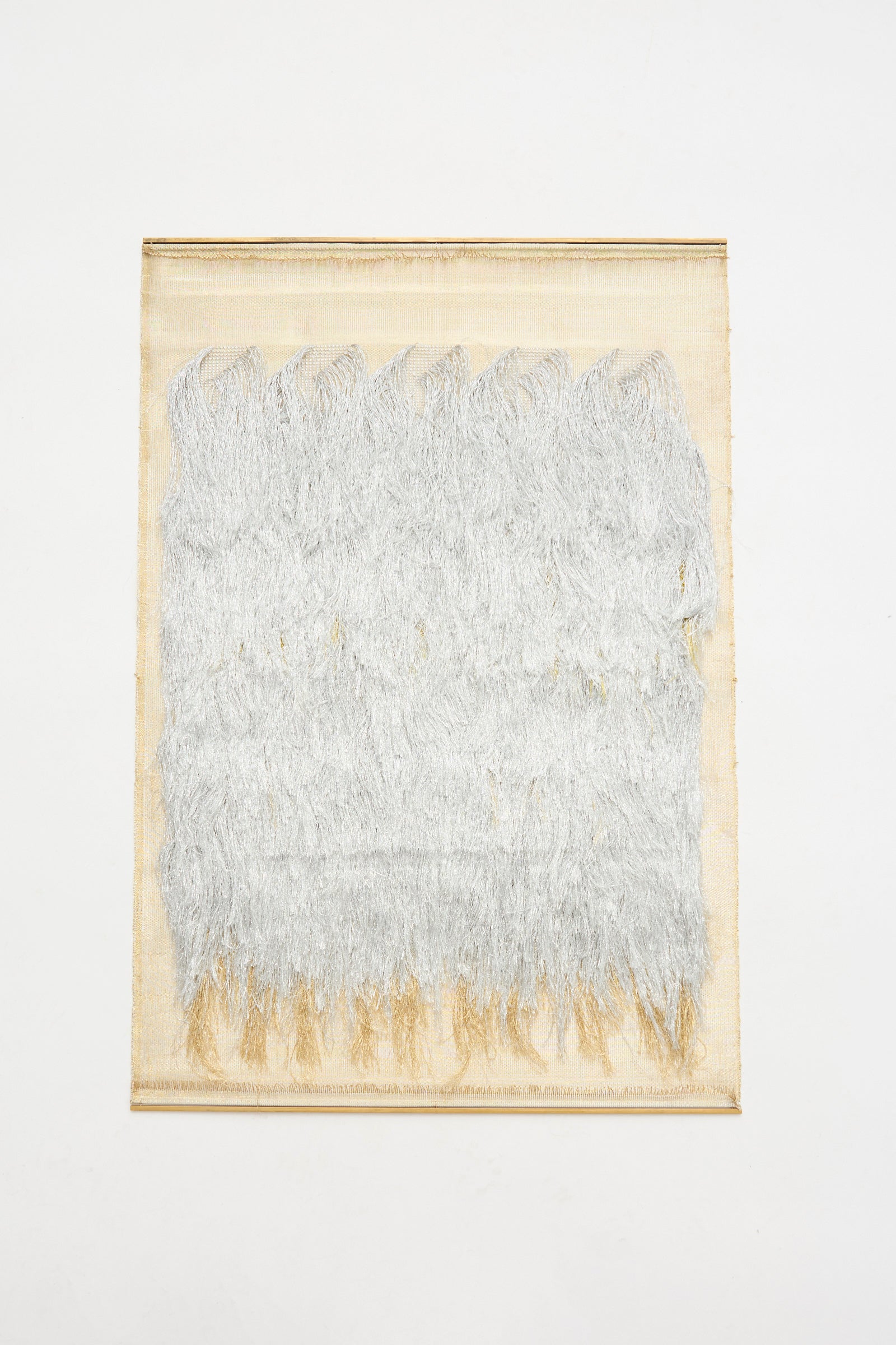 The Great Awakener Weaving by Justine Ashbee is a handmade UK wall hanging with a beige background and layered silver metallic fiber textures covering most of its rectangular surface.
