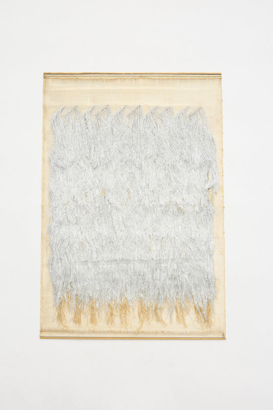 The Great Awakener Weaving by Justine Ashbee is a handmade UK wall hanging with a beige background and layered silver metallic fiber textures covering most of its rectangular surface.