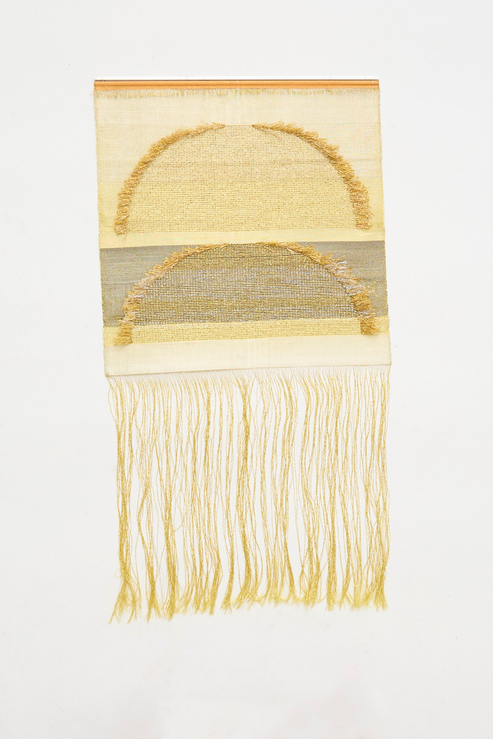 The Two Suns Rising Weaving by Justine Ashbee is a handmade UK wall hanging featuring tan semicircular woven patterns and long loose fringe at the bottom.