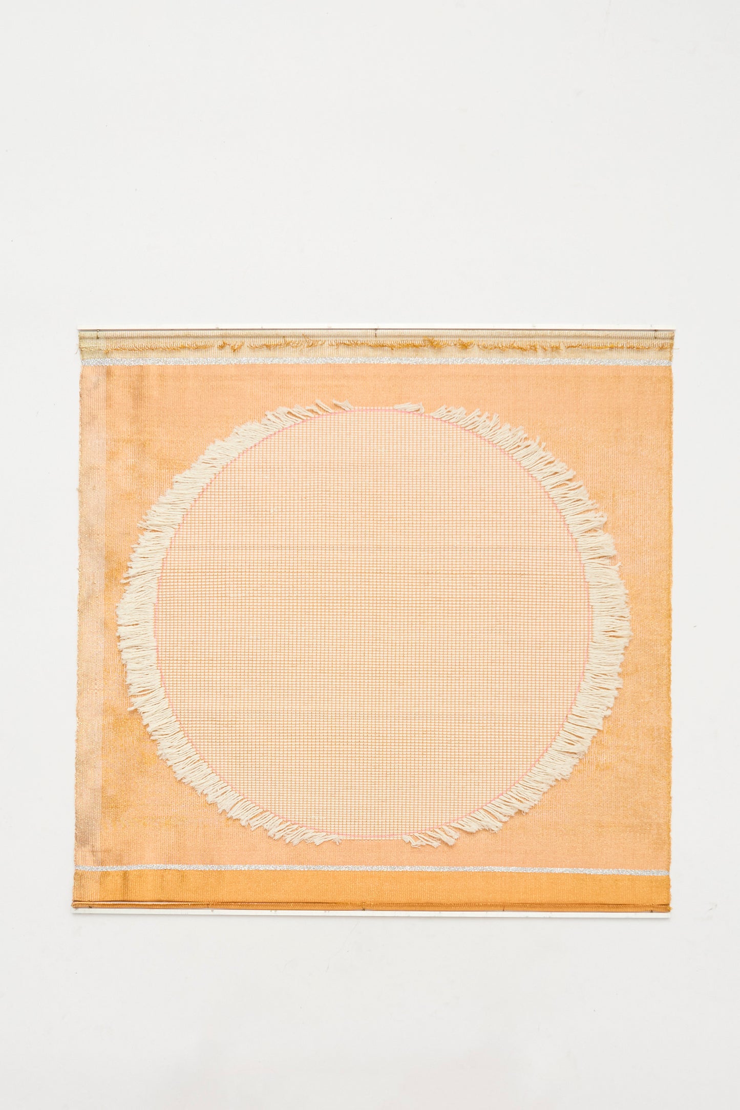 The White Moon Weaving by Justine Ashbee is a handmade square orange textile from the UK, showcasing a large off-white fringed circle in the center, displayed on a plain white background.